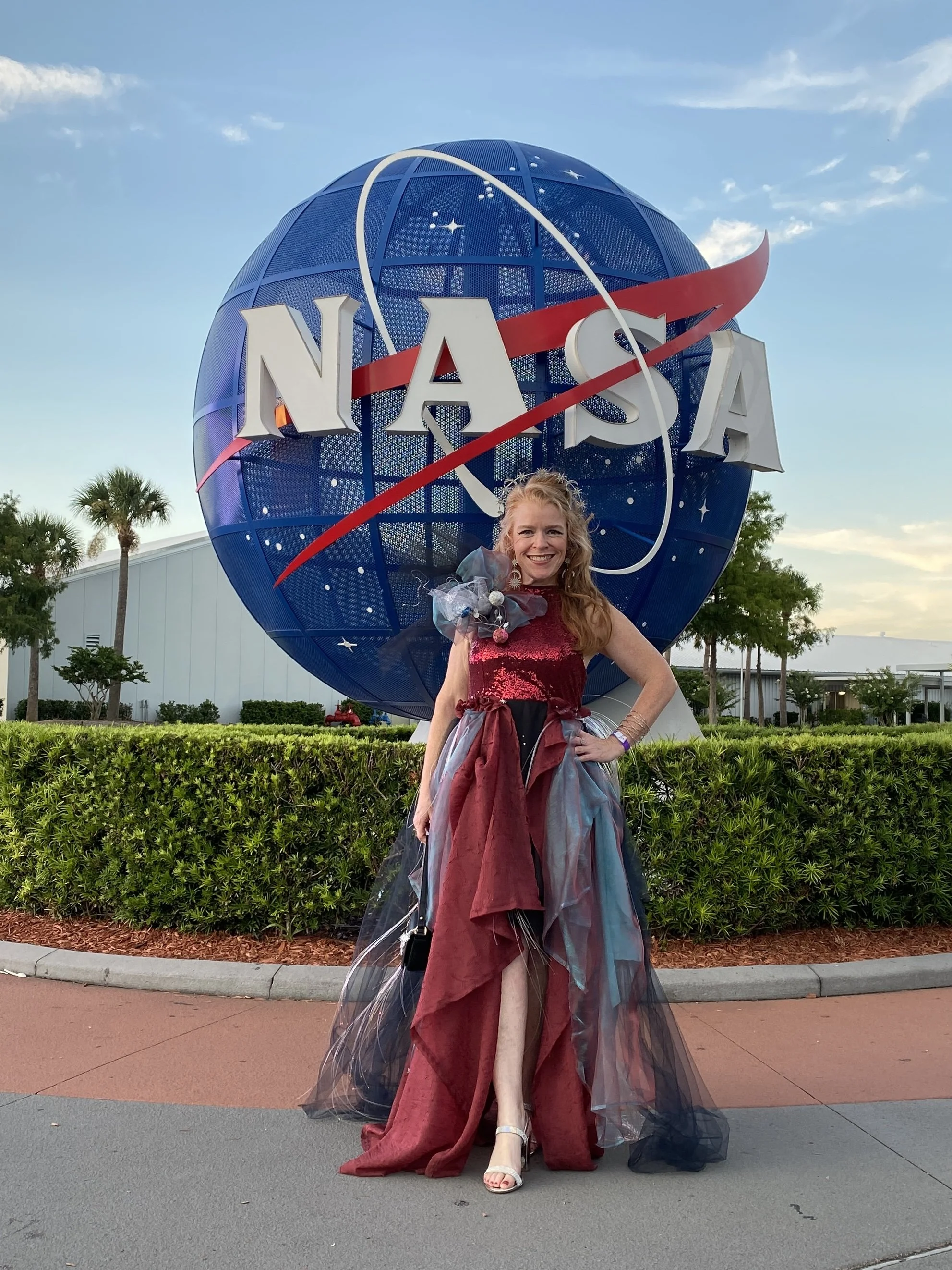 Nancy Coddington wearing a fiber optic dress she designed standing in front of NASA meatball logo.