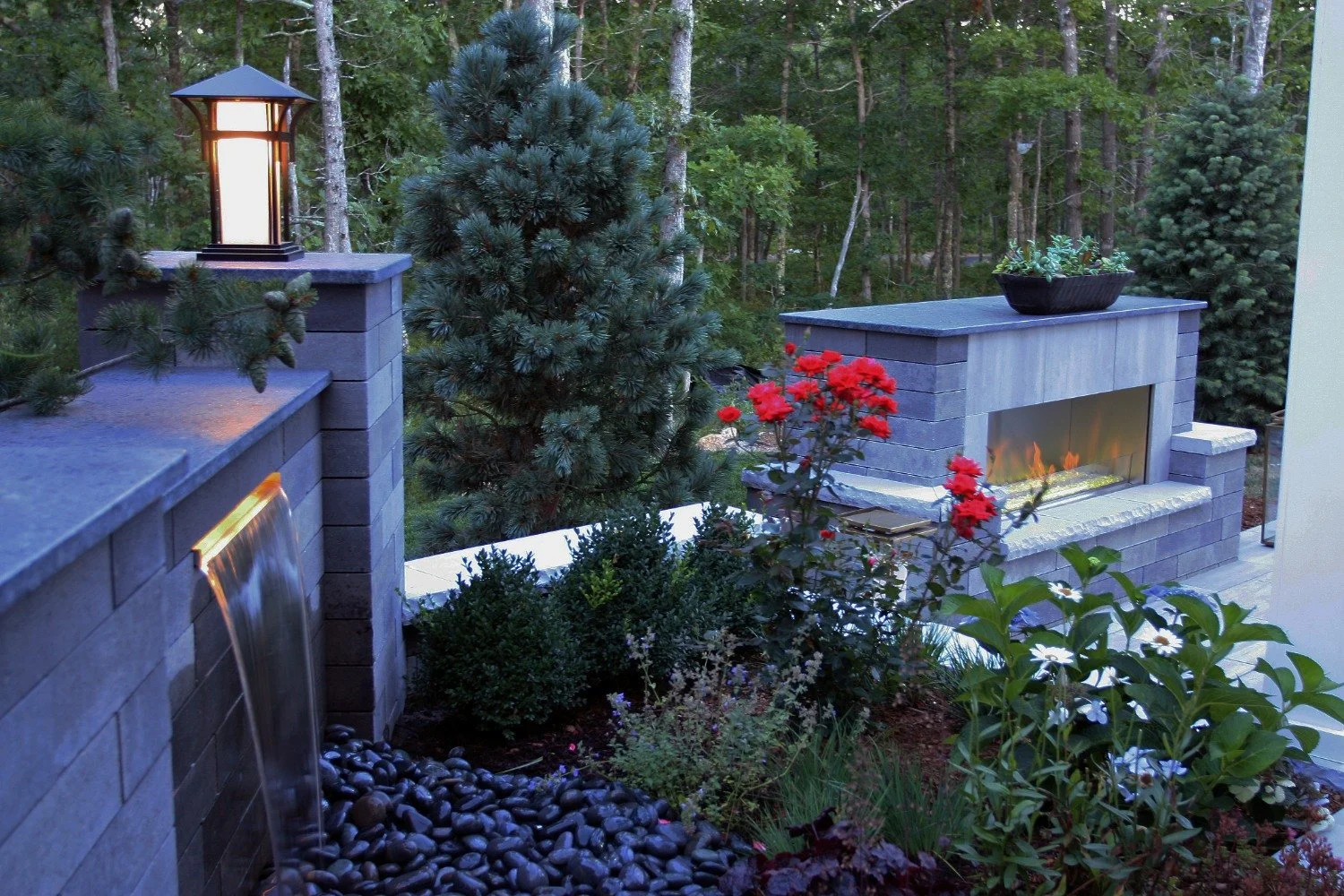 Water feature and outdoor fire place with flowers and green plantings