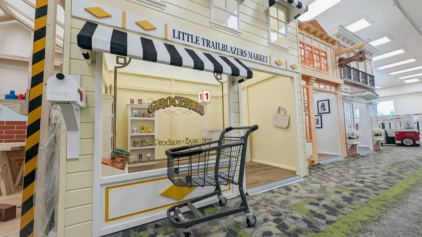 Toy storefront in an indoor play area designed to look like a small market with a shopping cart, colorful buildings, and playful decorations.