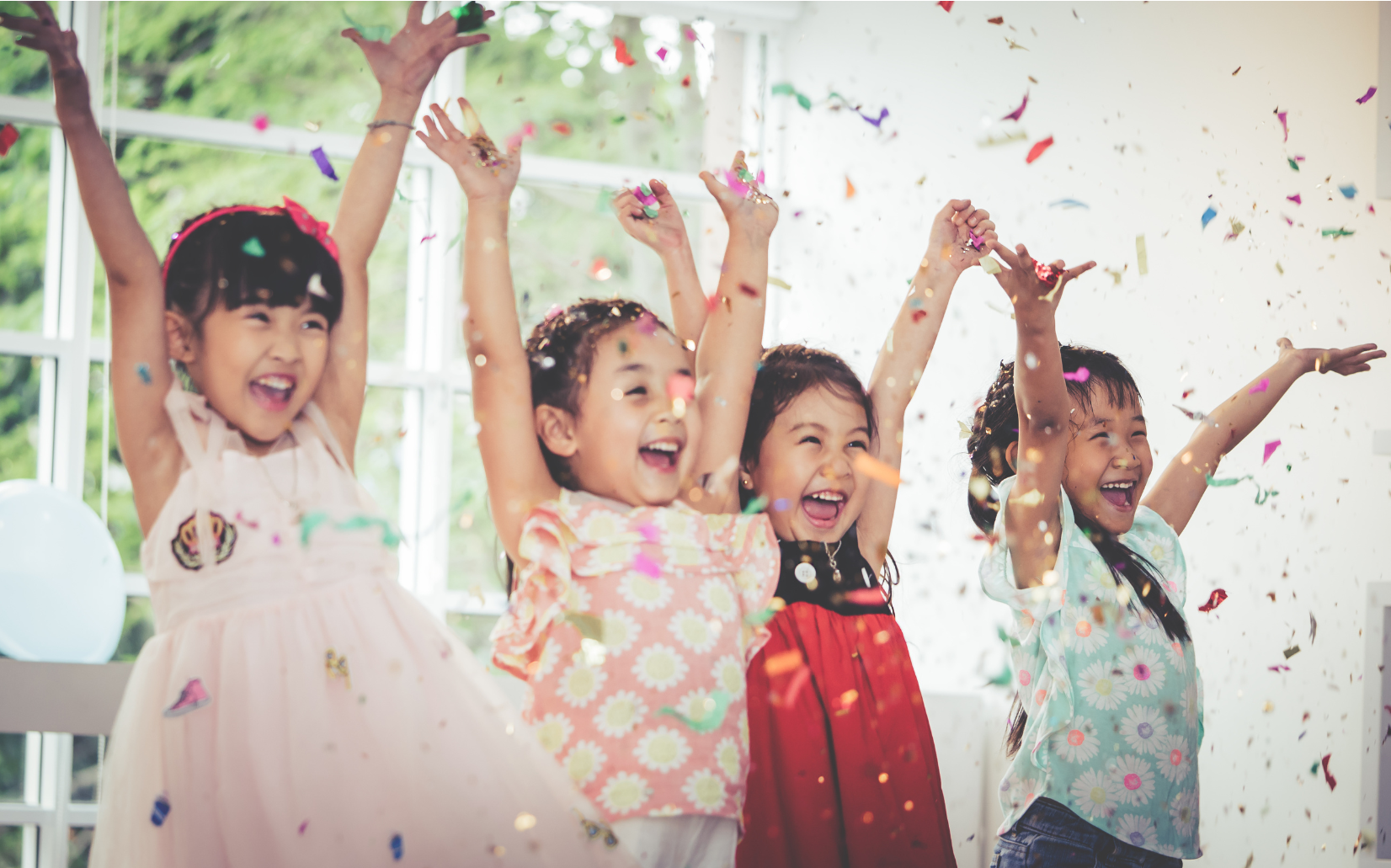 Four young girls celebrating with confetti in a bright and cheerful room.