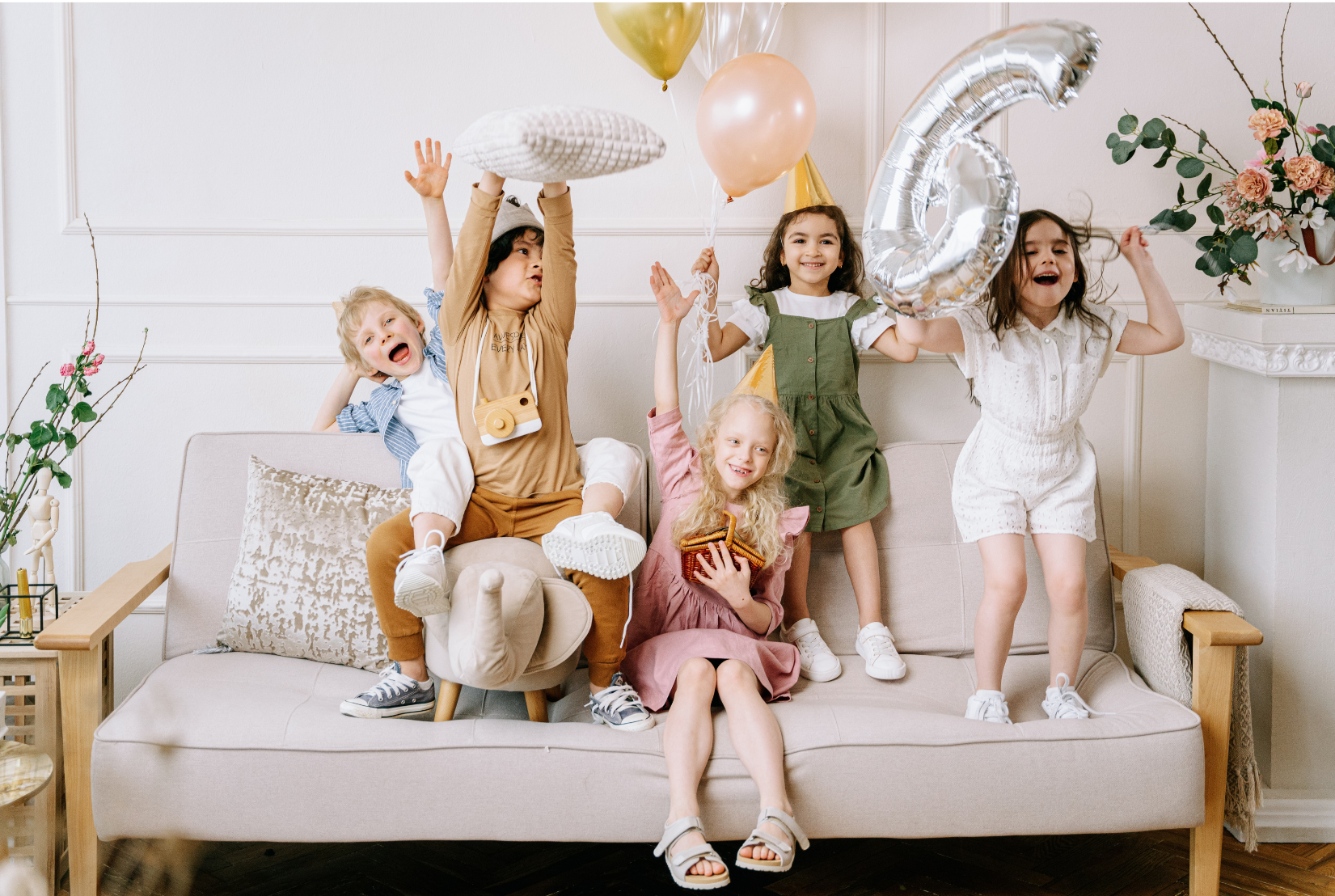 Group of children celebrating a birthday party, with balloons, party hats, and joyful expressions, in a living room.
