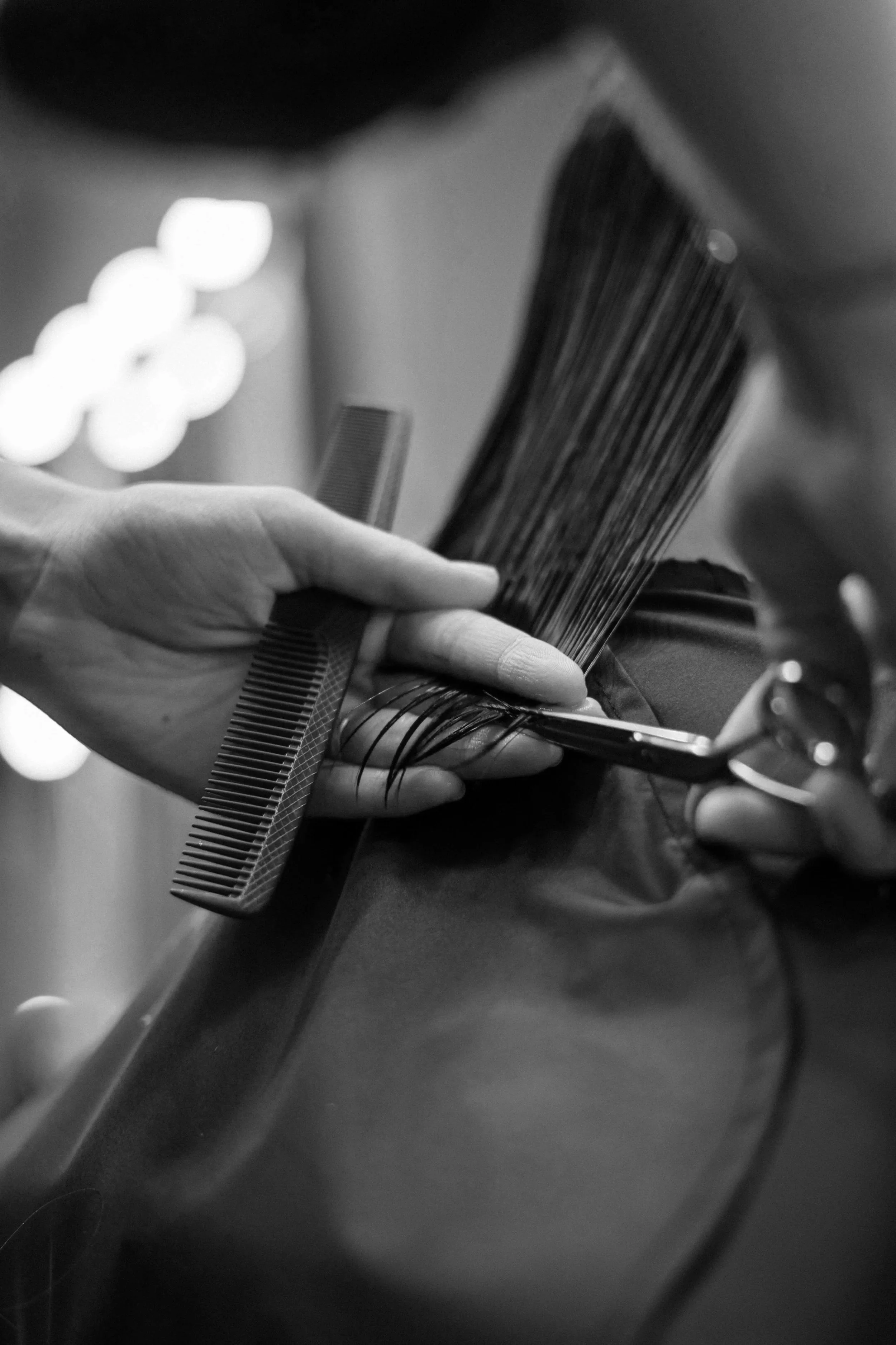 Une main tenant un peigne et une coiffure avec des cheveux noirs. L'image est en noir et blanc.