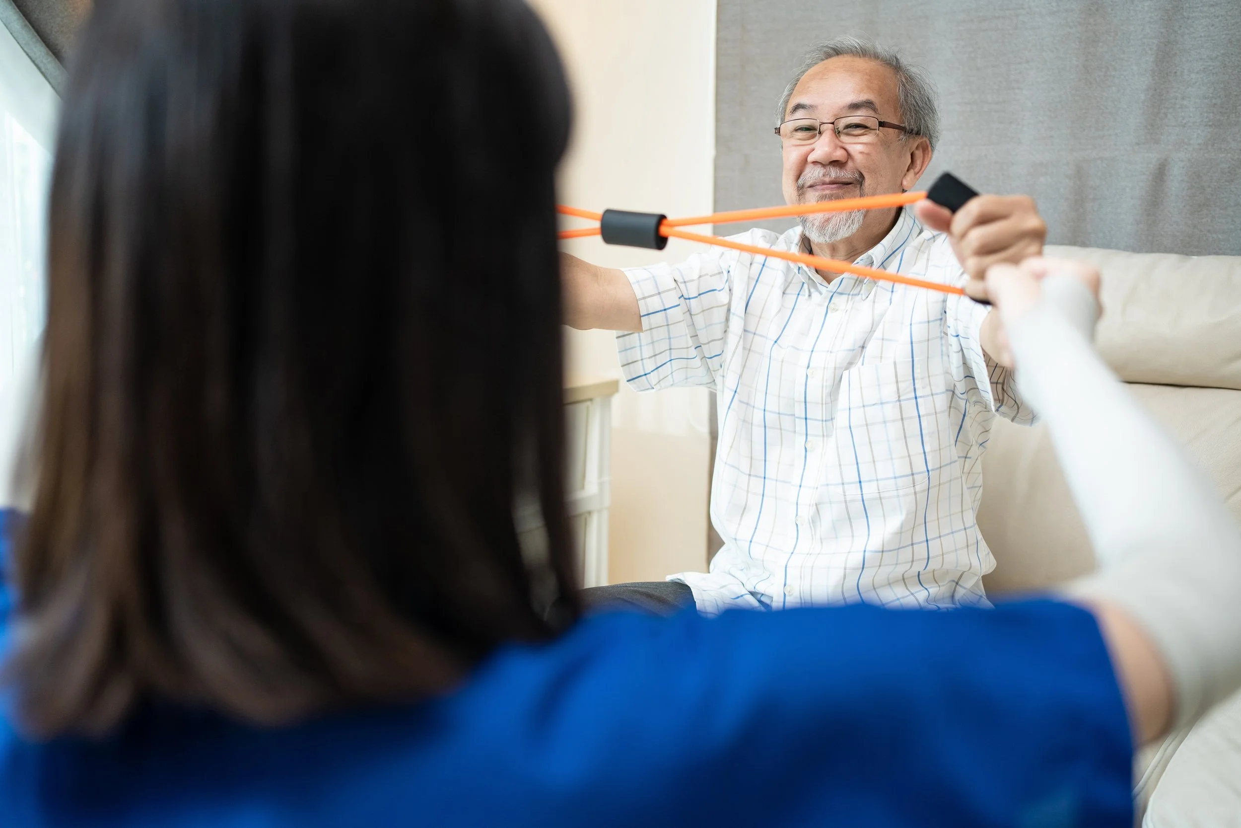 Gentleman using exercise band with his hands while supervised by support worker