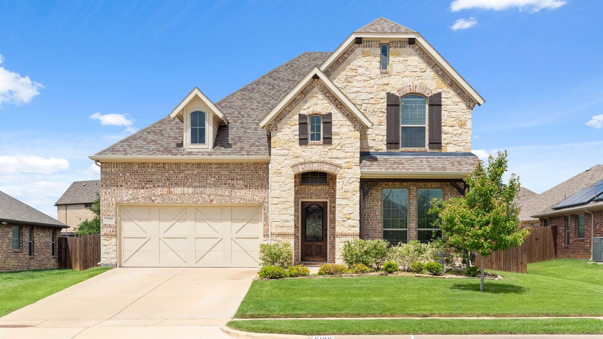 A two-story house with stone and brick exterior, a gabled roof, and a attached garage in a suburban neighborhood.