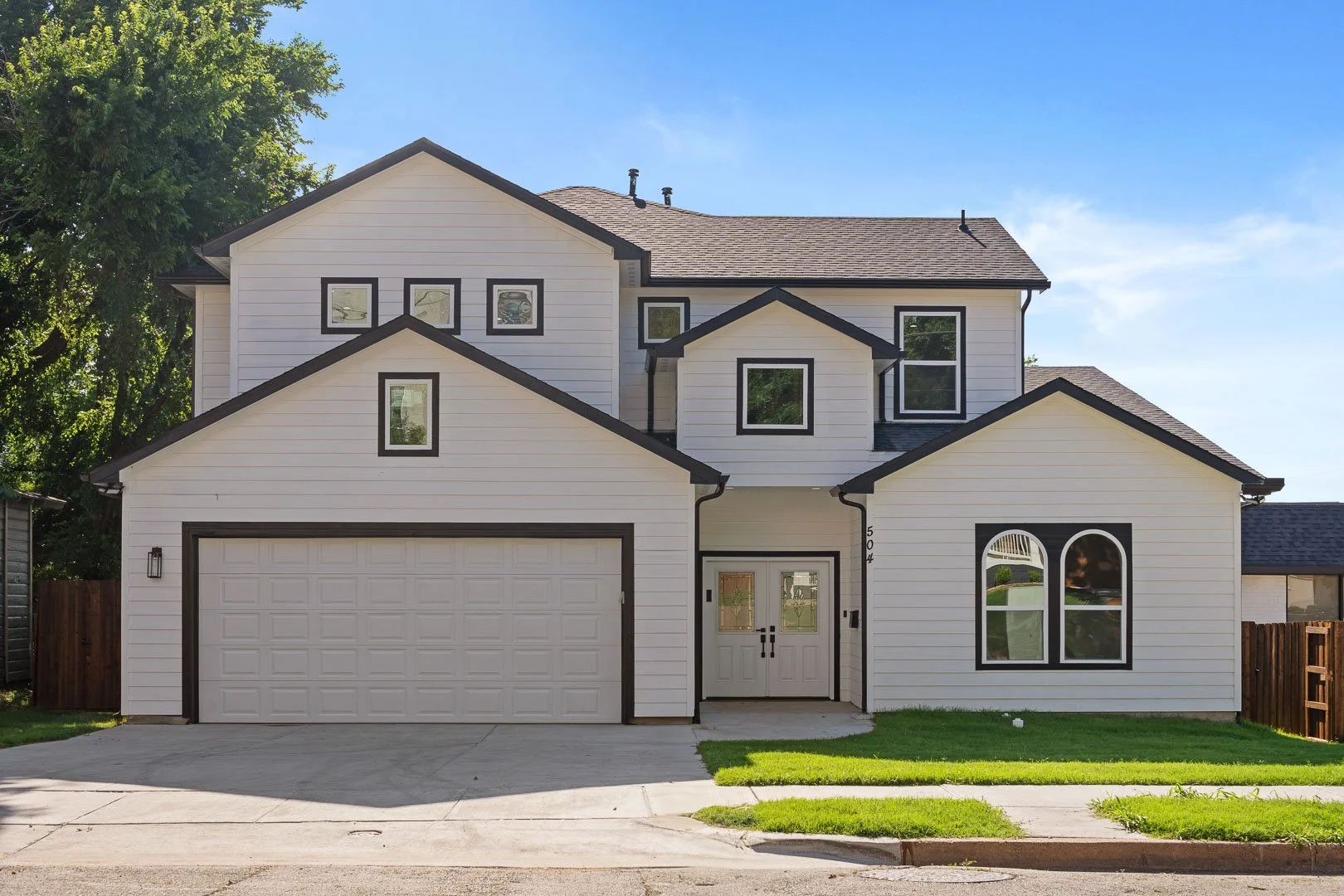 A modern two-story house with a white exterior and black trim, featuring a front garage, multiple windows, and a small front yard with grass.