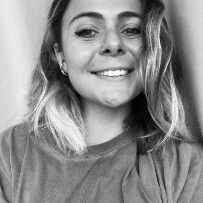Portrait d'une jeune femme souriante avec des cheveux longs et ondulés, portant un T-shirt