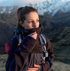 Femme en randonnée dans un paysage de montagnes, portant un manteau foncé et un sac à dos.