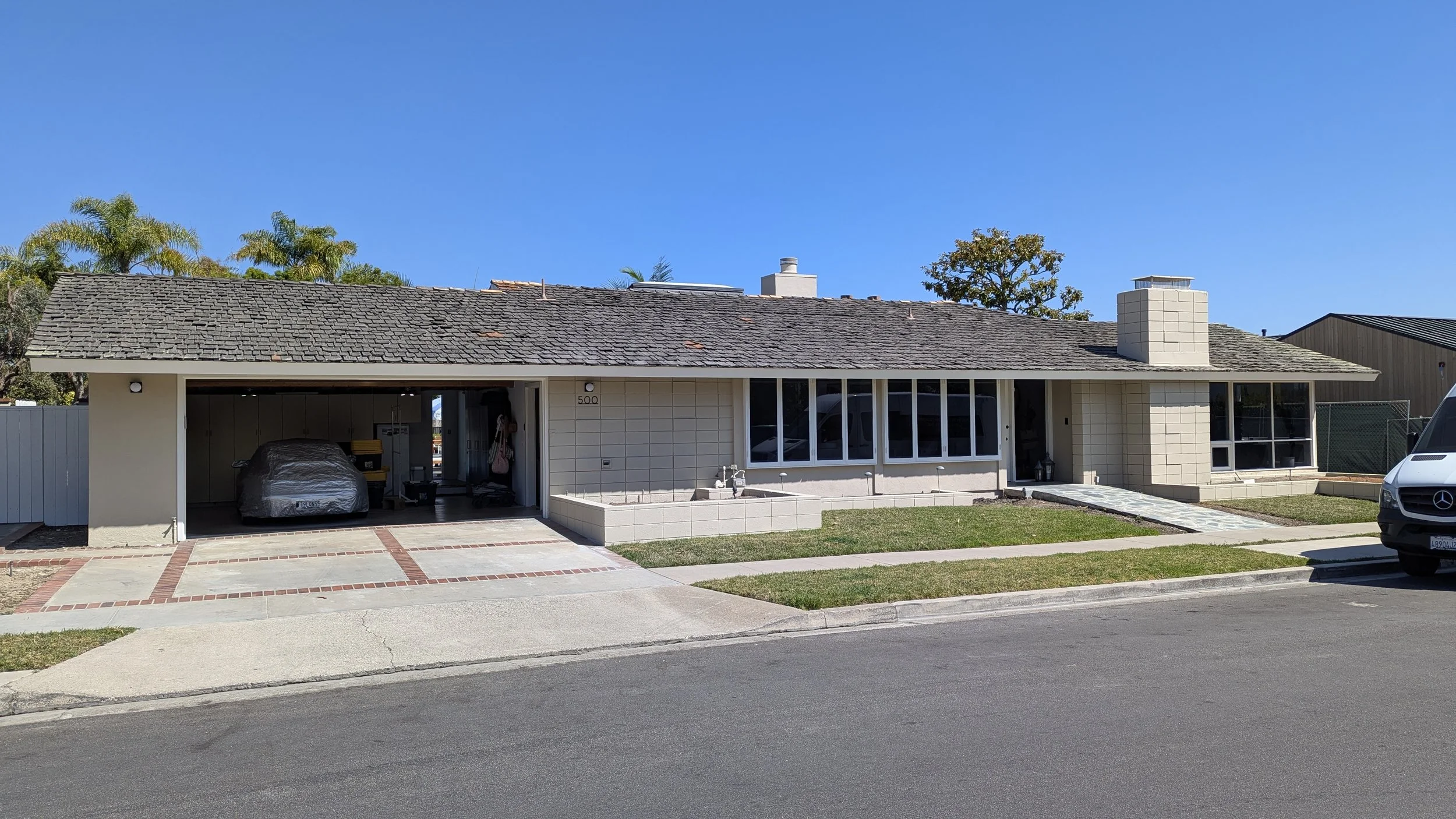 A single-story house with a garage, large windows, a chimney, and a walkway with a small lawn in front.