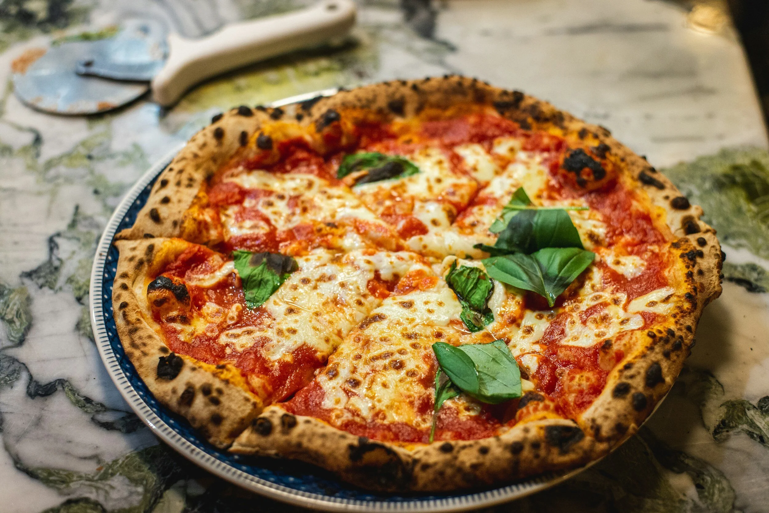 A freshly baked pepperoni pizza with basil leaves on a patterned plate on a marble table.