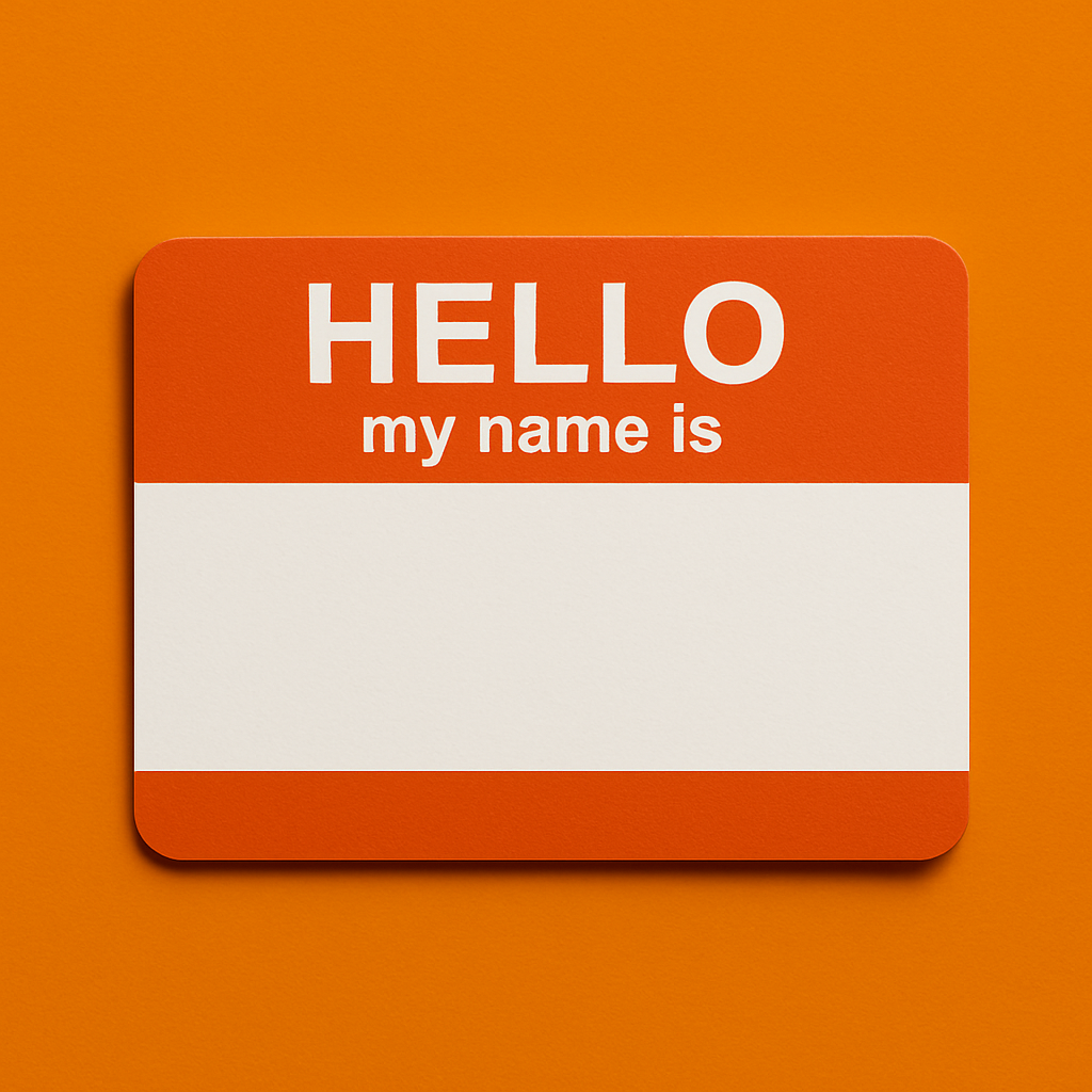 Orange and white name tag with the text 'HELLO my name is' at the top and a blank space below for writing a name, attached to an orange wall.