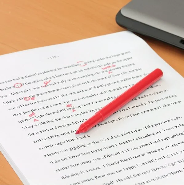 Open book with red pen resting on it, on a wooden surface