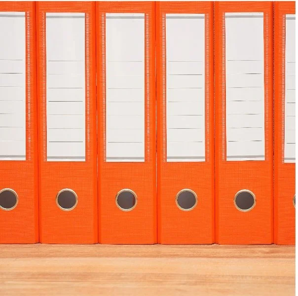 A row of orange plastic file binders with circular label holders on a wooden surface.