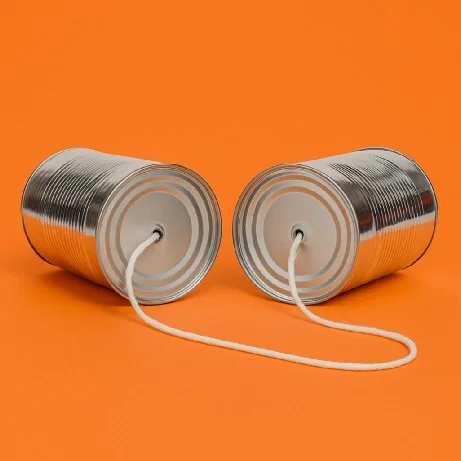 Two tin cans connected by a string against an orange background.