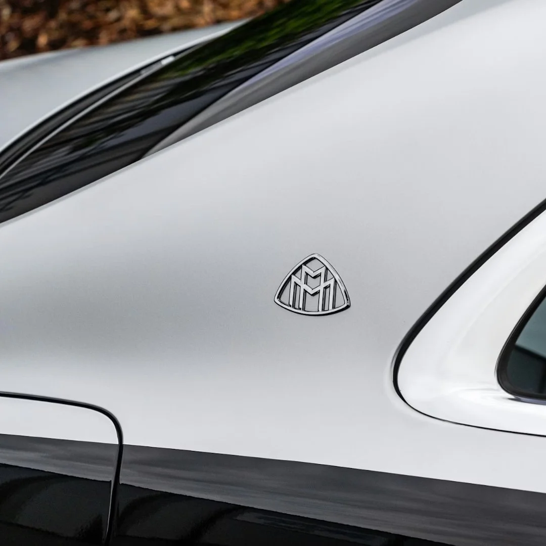 Close-up of a silver car with a triangular emblem that has a stylized M and M design on the hood.
