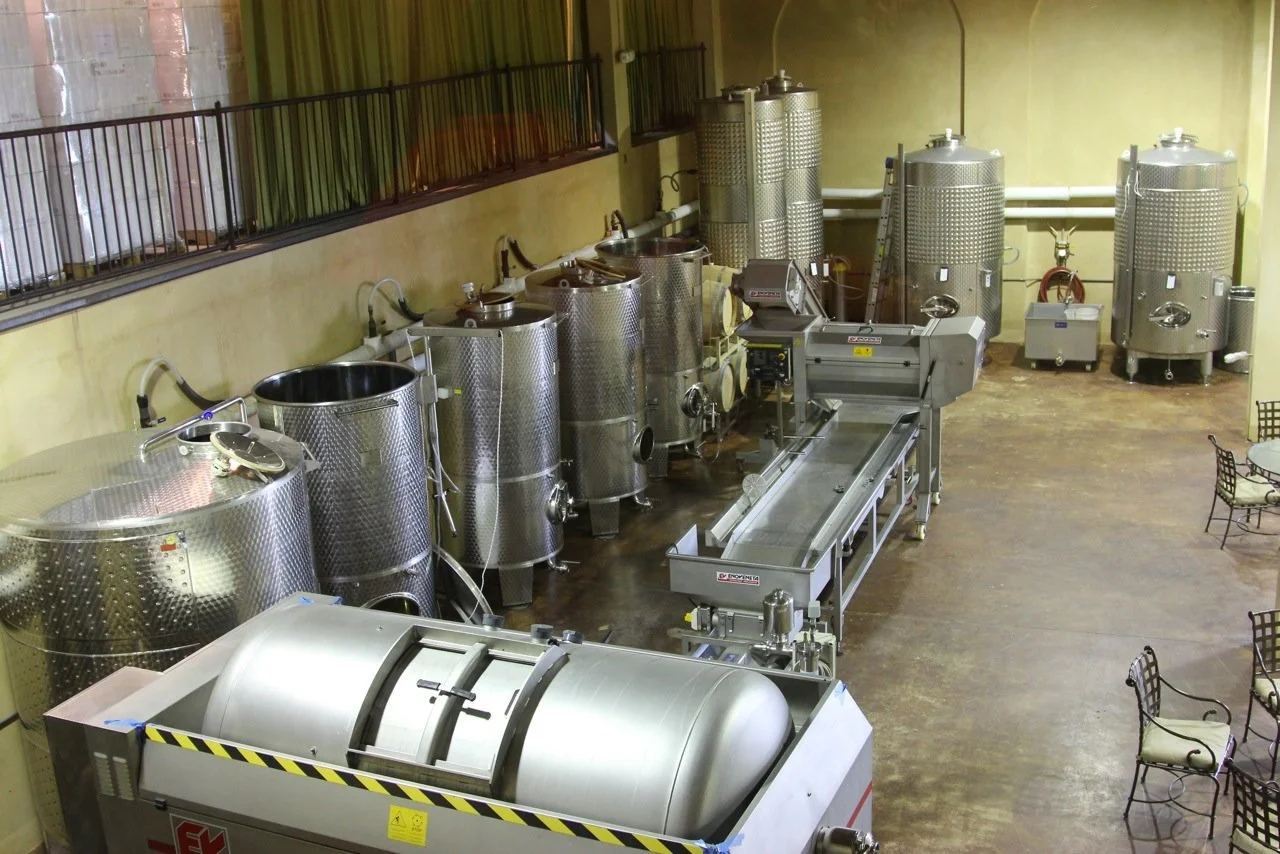 Commercial winery or brewing facility with large stainless steel fermentation tanks and processing equipment.