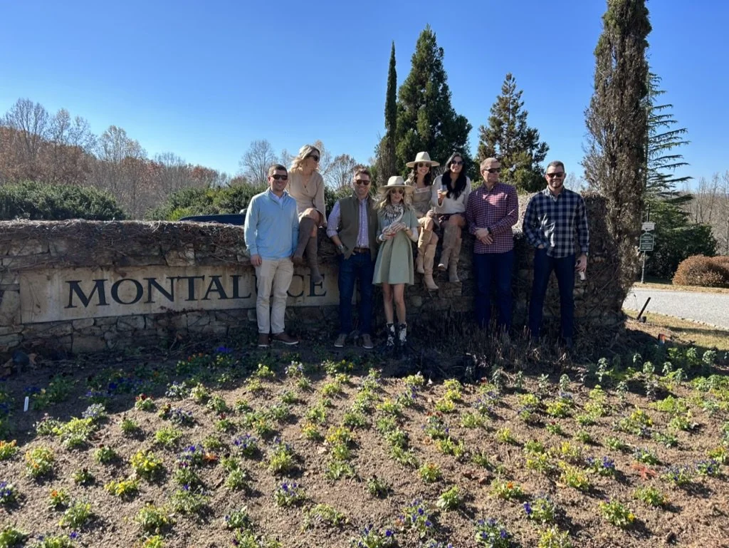 Group of people standing in front of a stone sign that reads 'Montlake,' with plants and trees in the background on a sunny day.