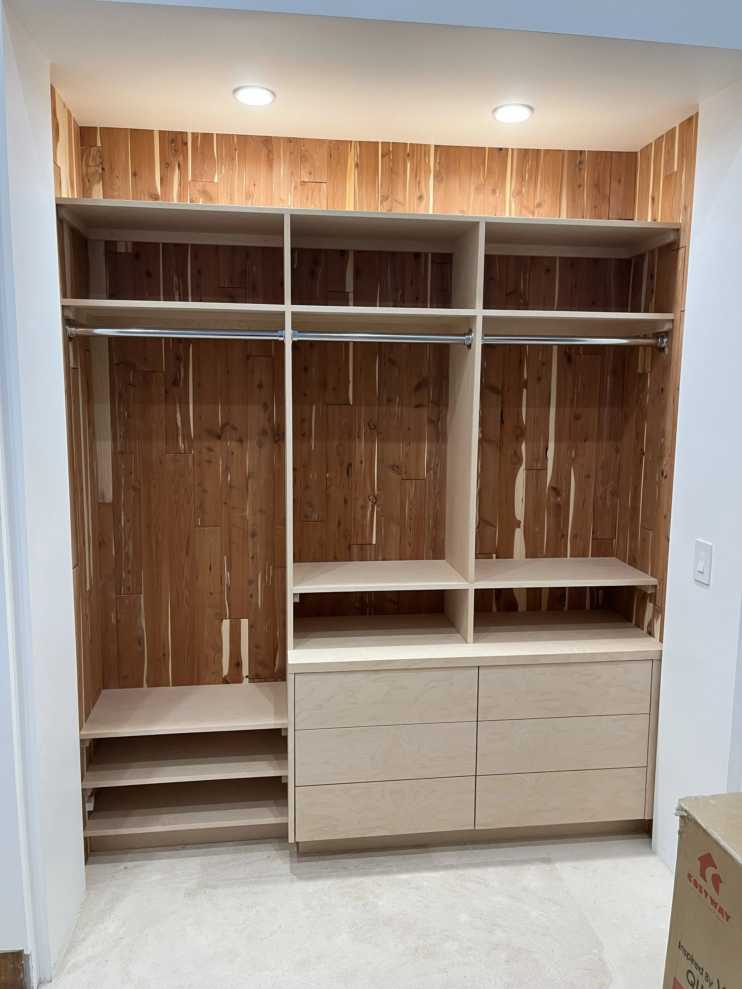 Empty closet with wooden interior, metal rods, and shelves, with built-in drawers at the bottom.