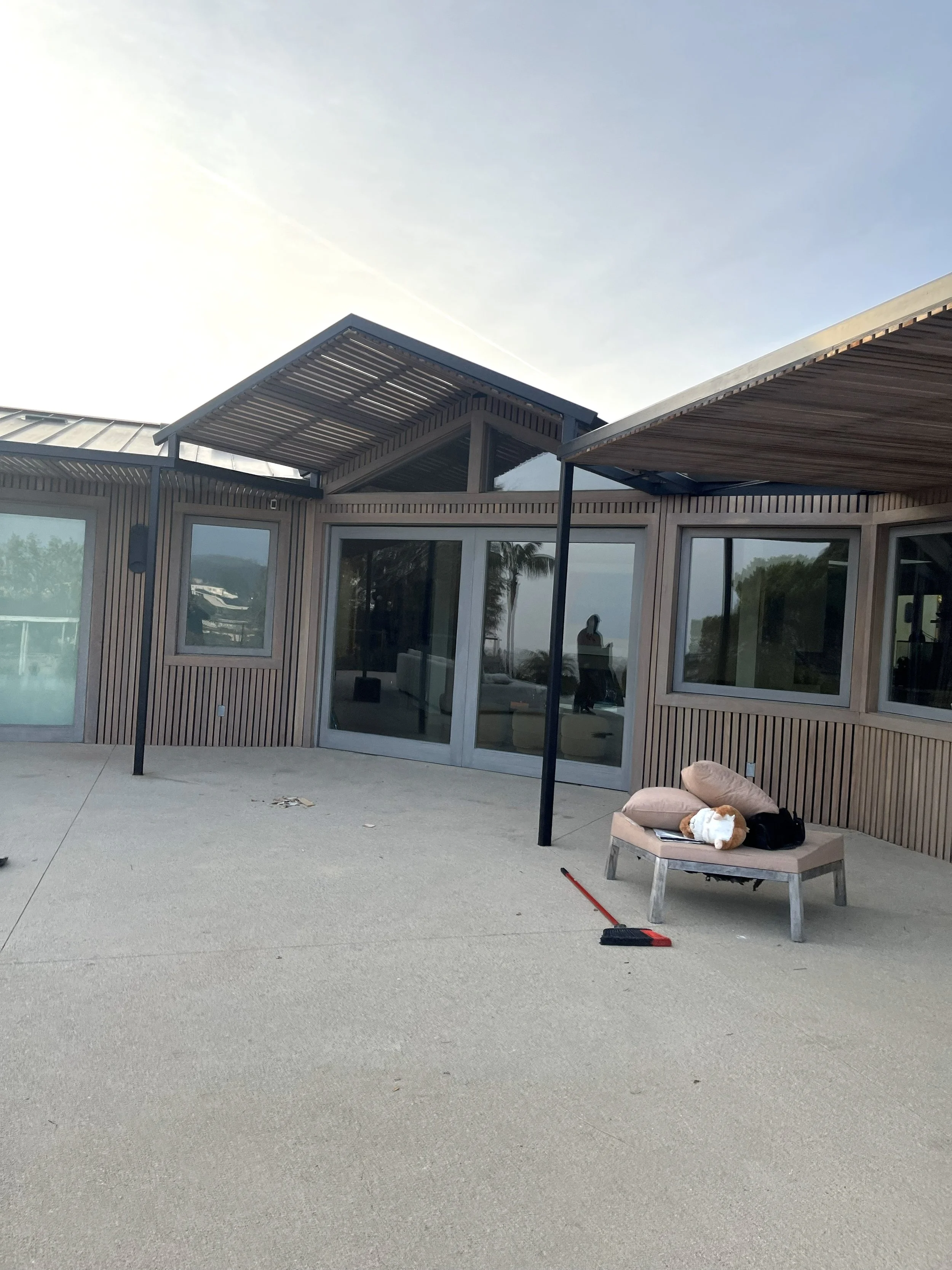 Modern house exterior with wooden siding, large glass sliding door, patio furniture, and a broom on the patio