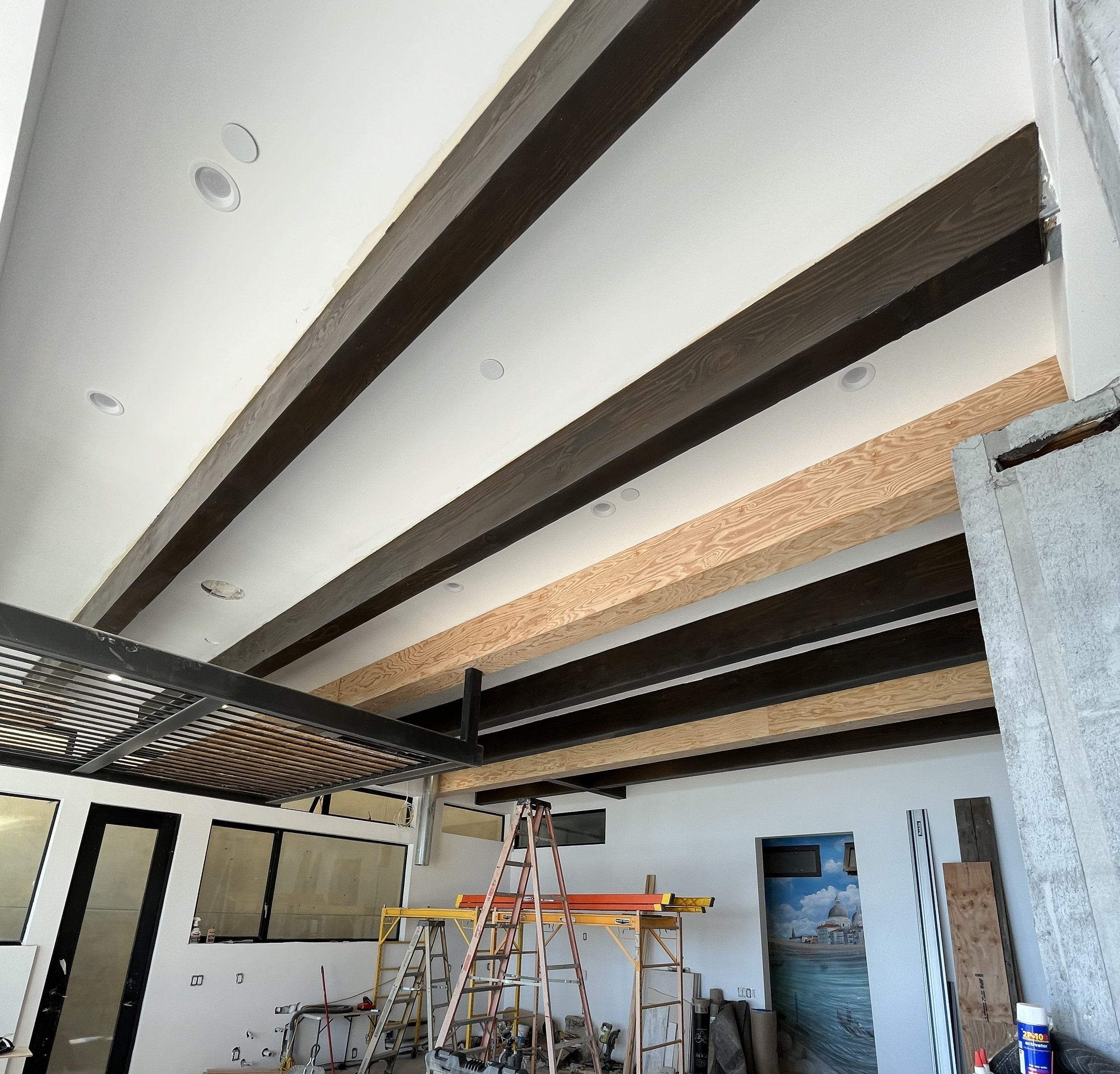 Interior construction site with exposed ceiling beams, scaffolding, and various tools and materials.