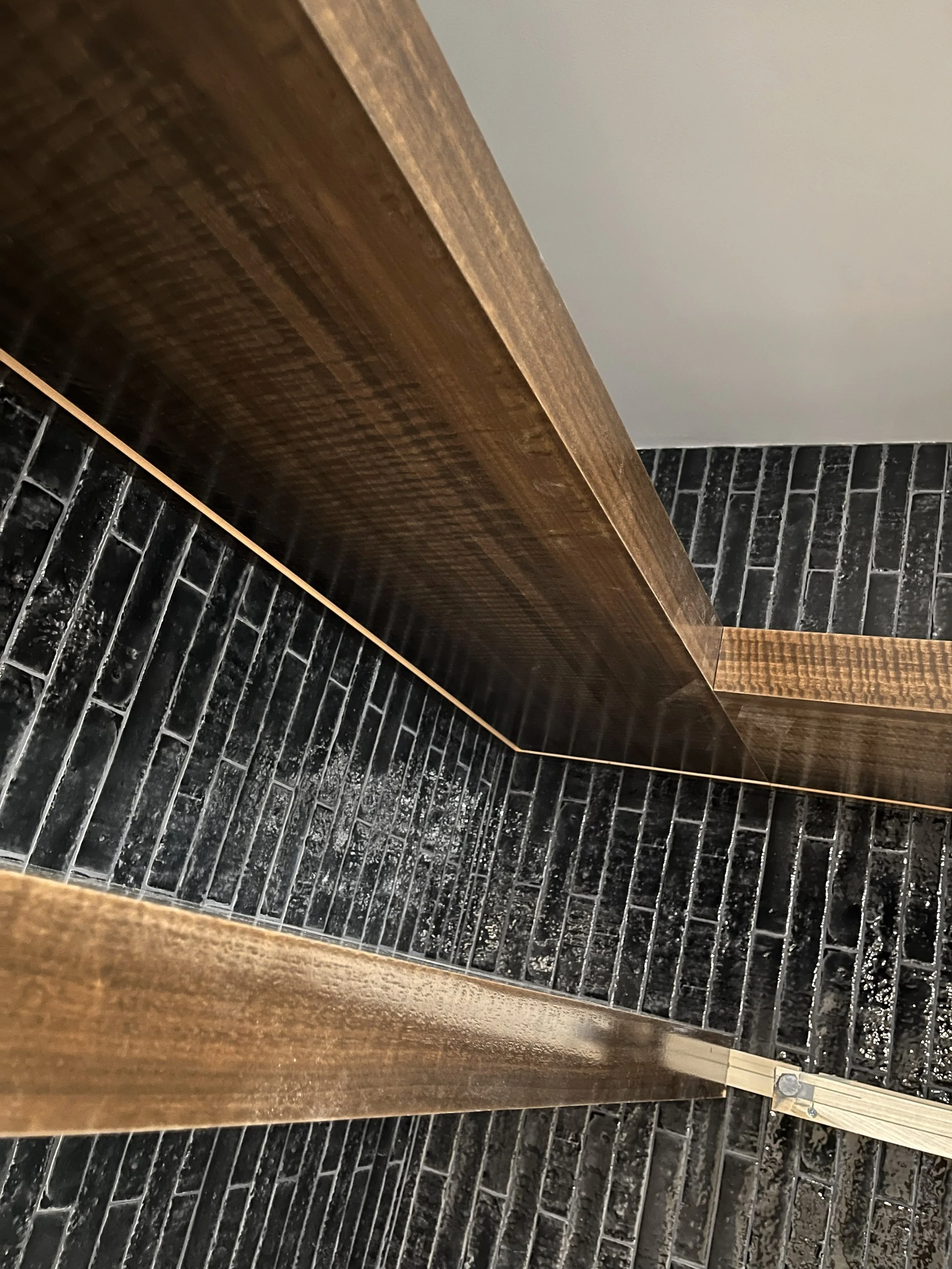 Close-up of wooden trim and a black brick wall with mortar lines in a room interior.