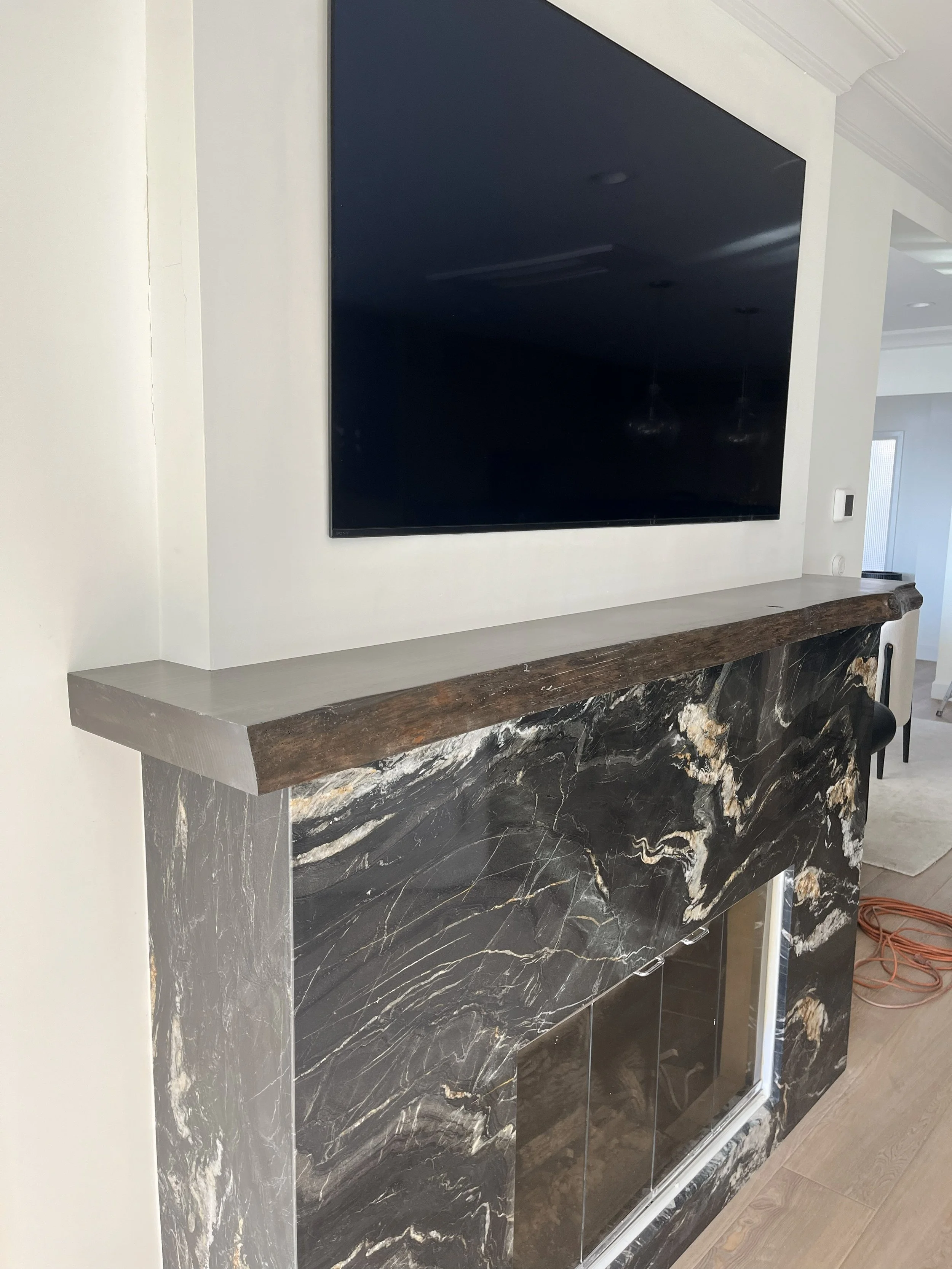 A flat-screen TV mounted above a modern fireplace with a black marble surround and a wooden mantel in a living room.