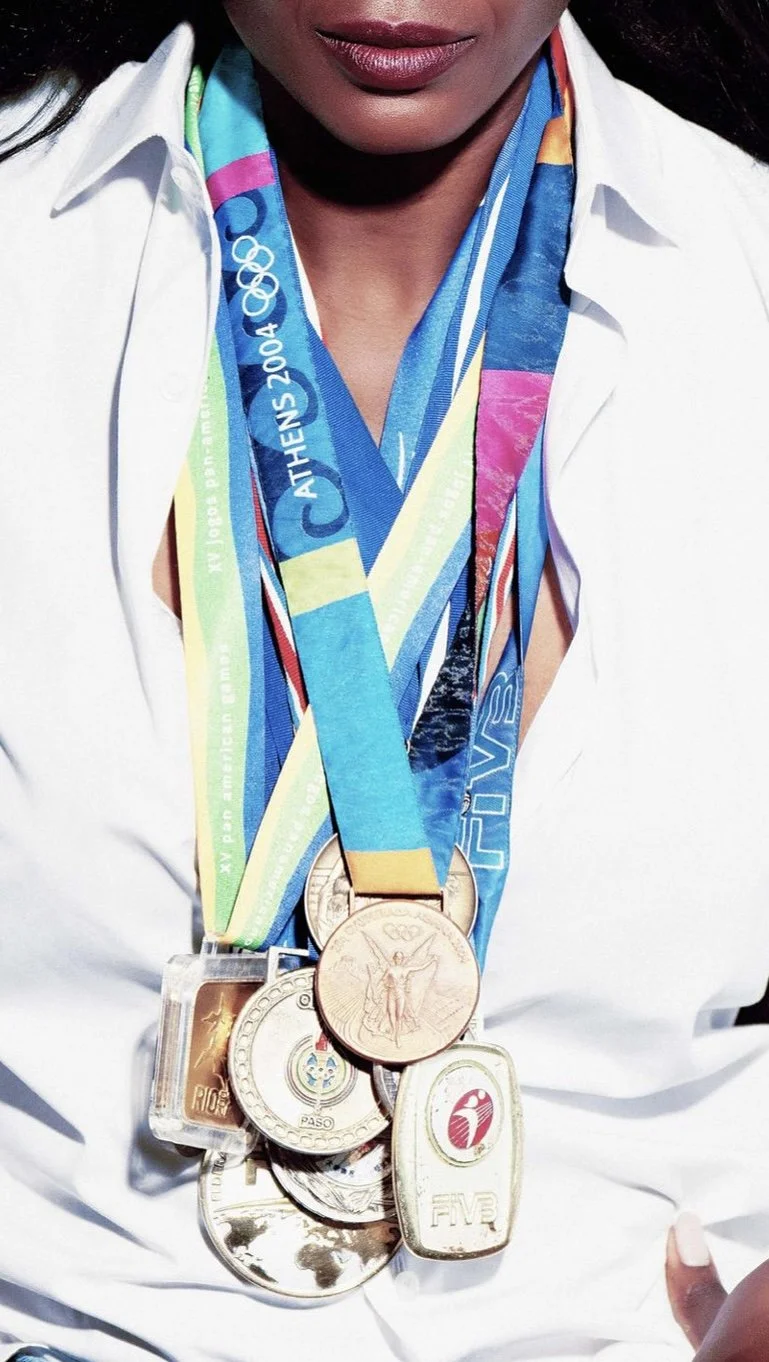 Close-up of a woman wearing multiple Olympic medals around her neck, with a white shirt and a colorful fabric lanyard, celebrating her achievements.