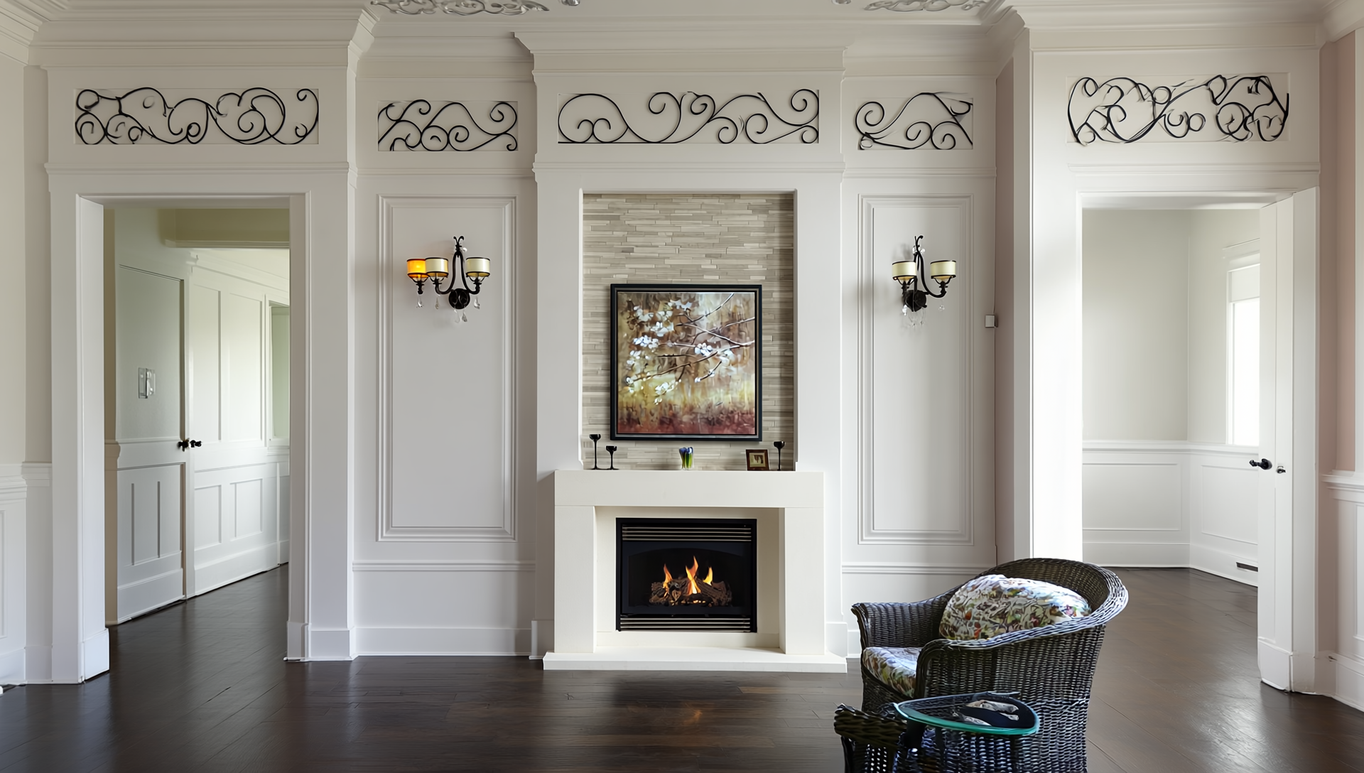 Living room with white walls, dark hardwood floors, a fireplace with a fire, a framed artwork above it, black and yellow wall sconces, decorative wrought iron panels above doorways, a wicker chair with a floral cushion, and a small glass side table.