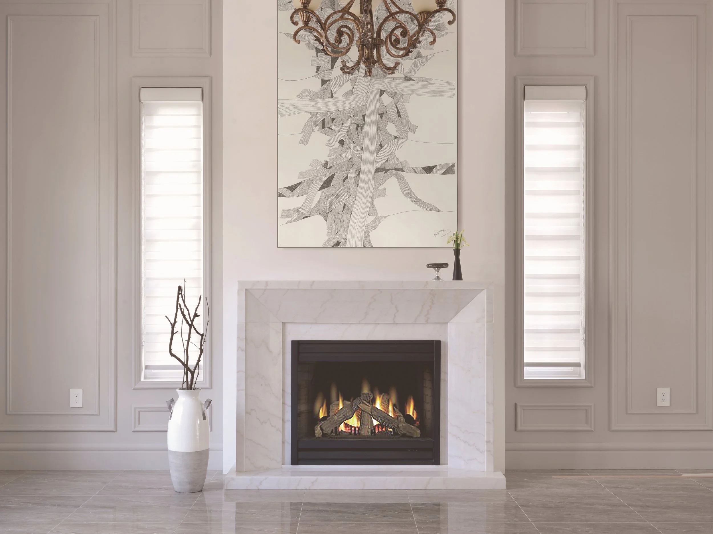 Modern living room with a fireplace, two tall vertical windows with blinds, a large abstract art piece above the fireplace, a white vase with branches to the left, and a small vase with a flower on the mantel.