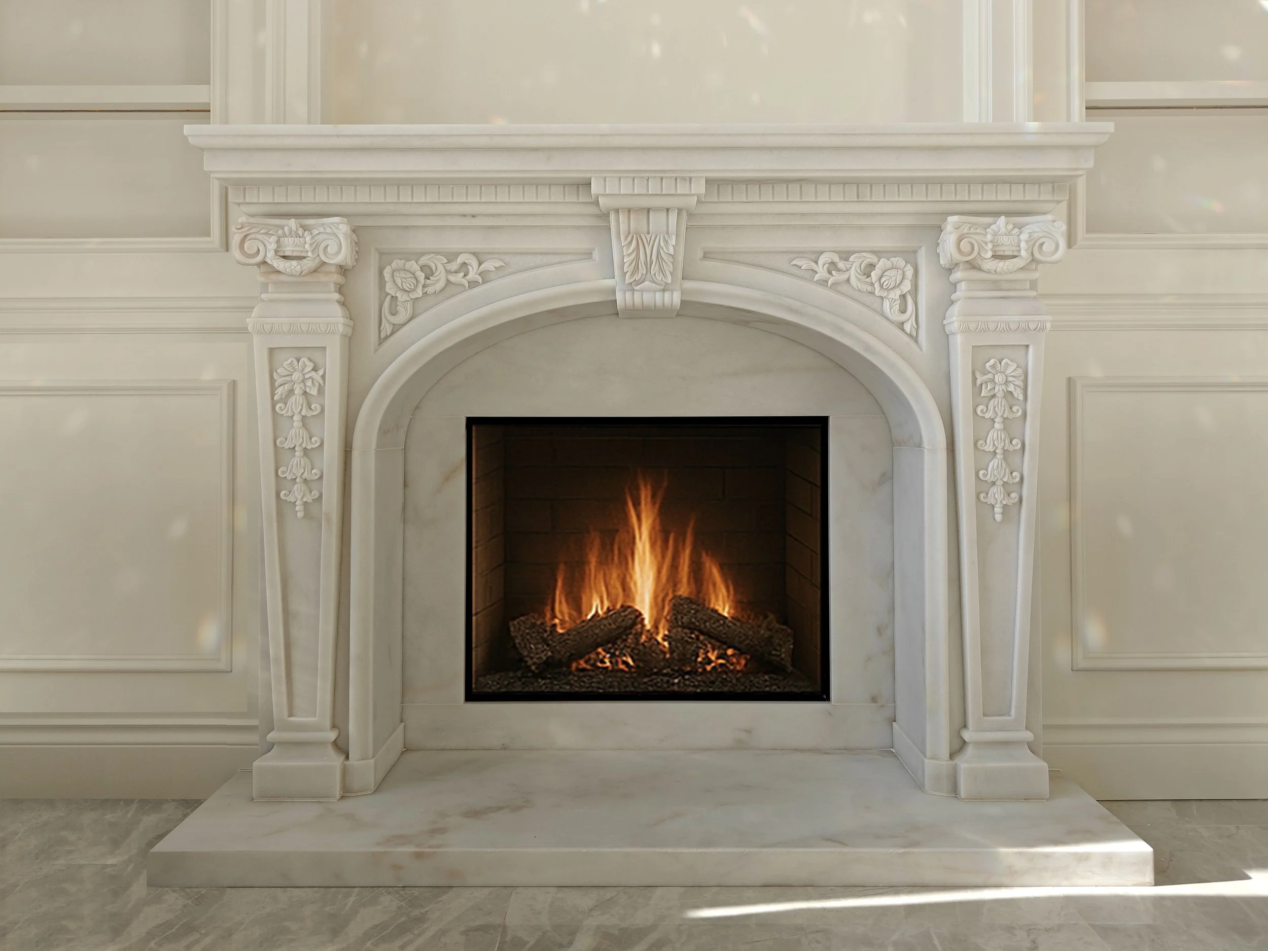 White marble fireplace with intricate carvings, fire burning inside, set in a decorated wall with paneling, and a marble hearth in front.