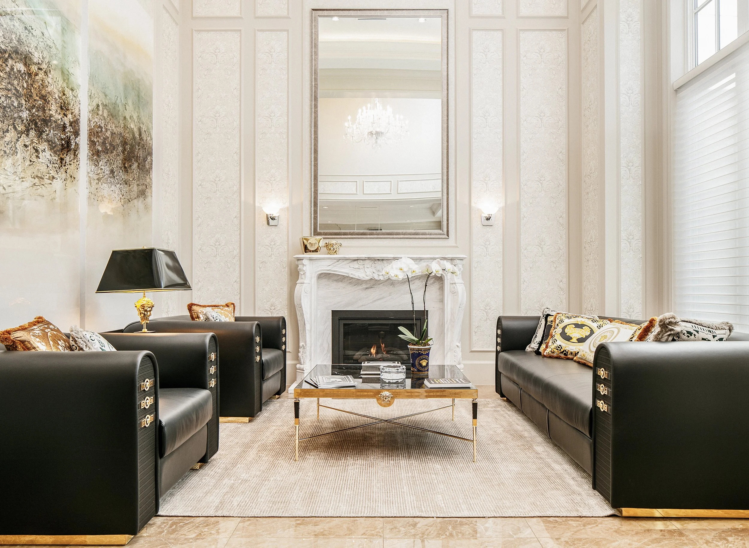 Elegant living room with black leather sofas, a marble fireplace, a glass coffee table, decorative pillows, and a large mirror above the fireplace.