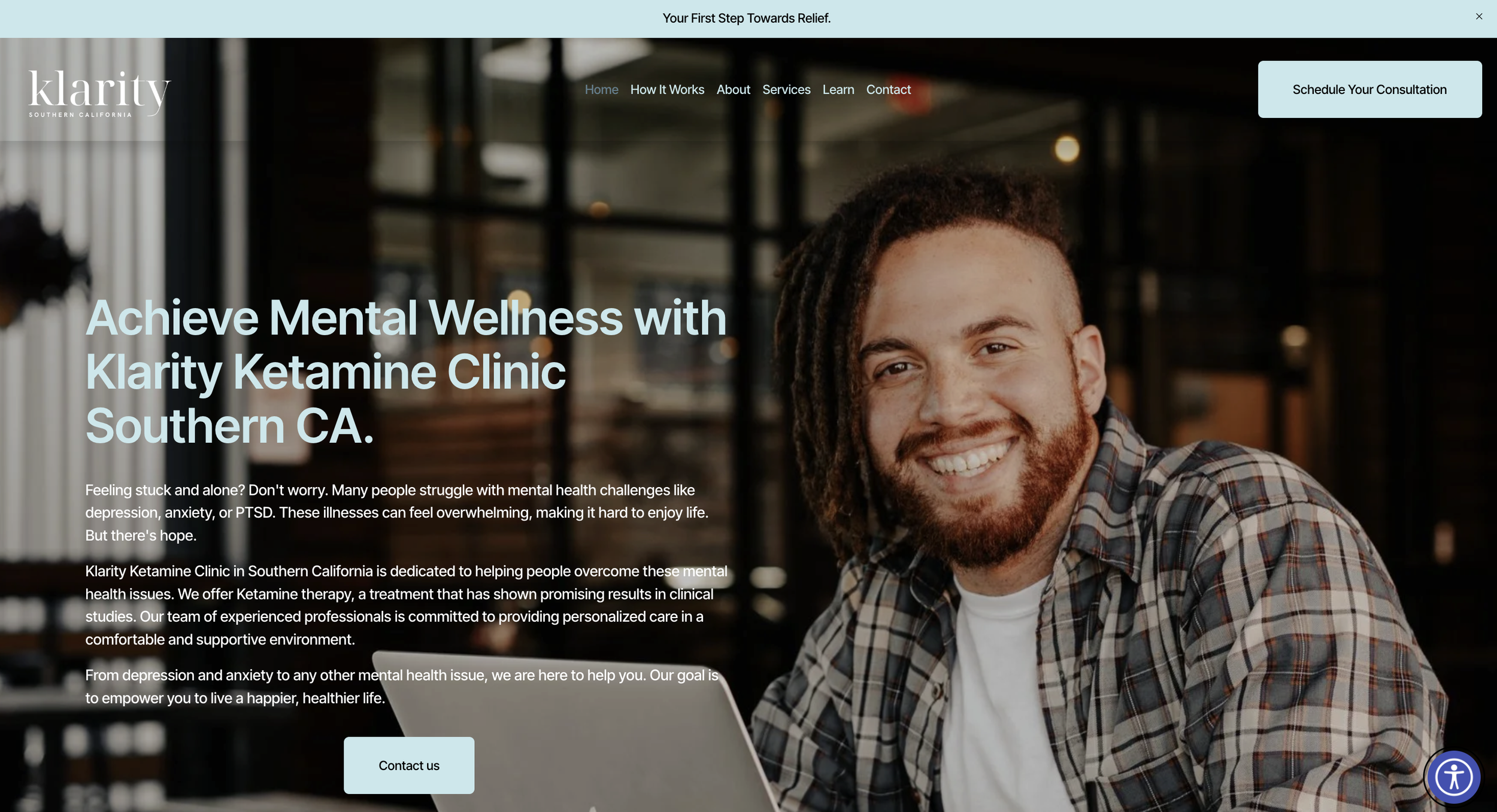 Smiling man with dreadlocks and beard in a plaid shirt working on a laptop at a mental health clinic website homepage.