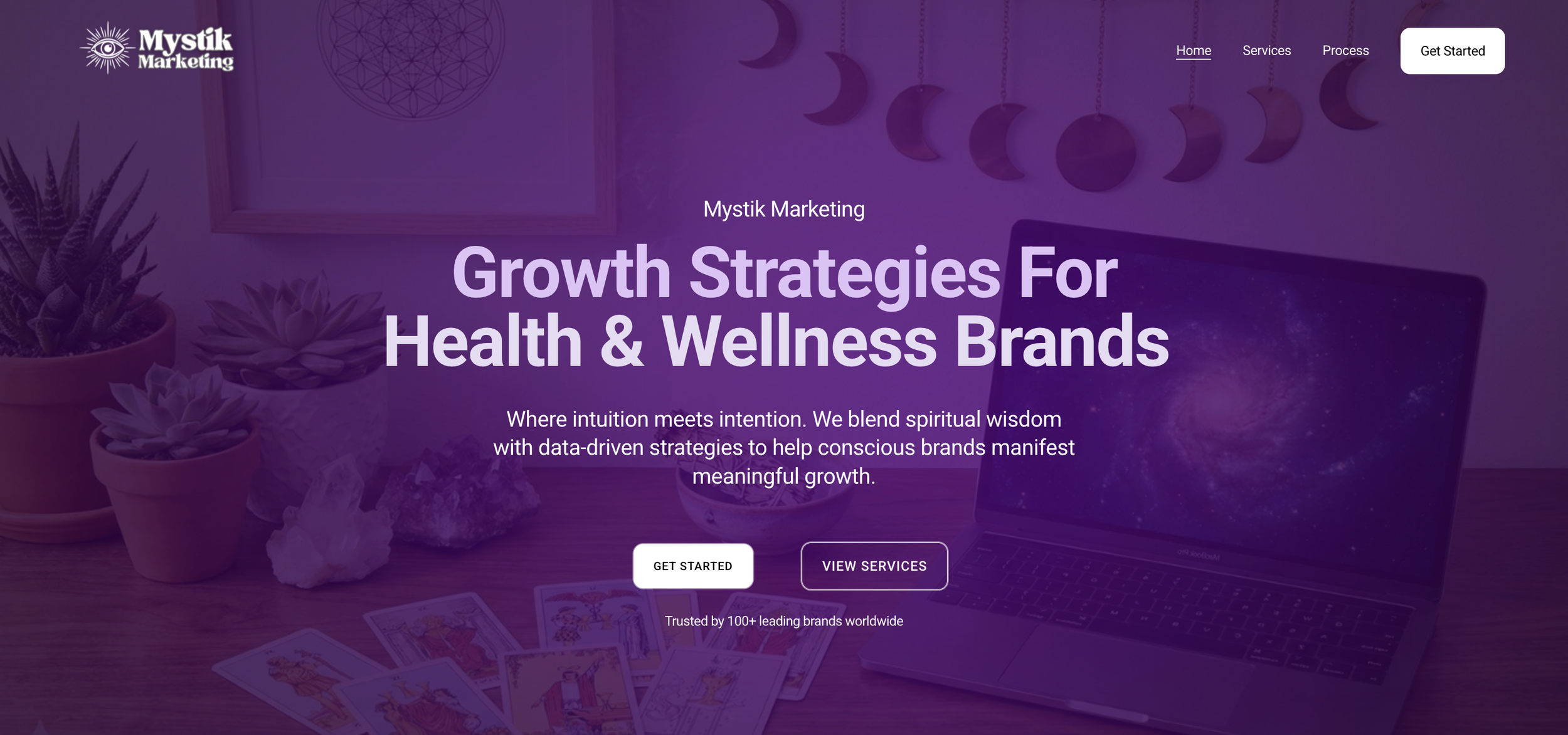 Homepage of Mystik Marketing website with a purple-themed background, featuring a laptop, tarot cards, potted plants, and moon phase decorations, along with text about growth strategies for health and wellness brands.