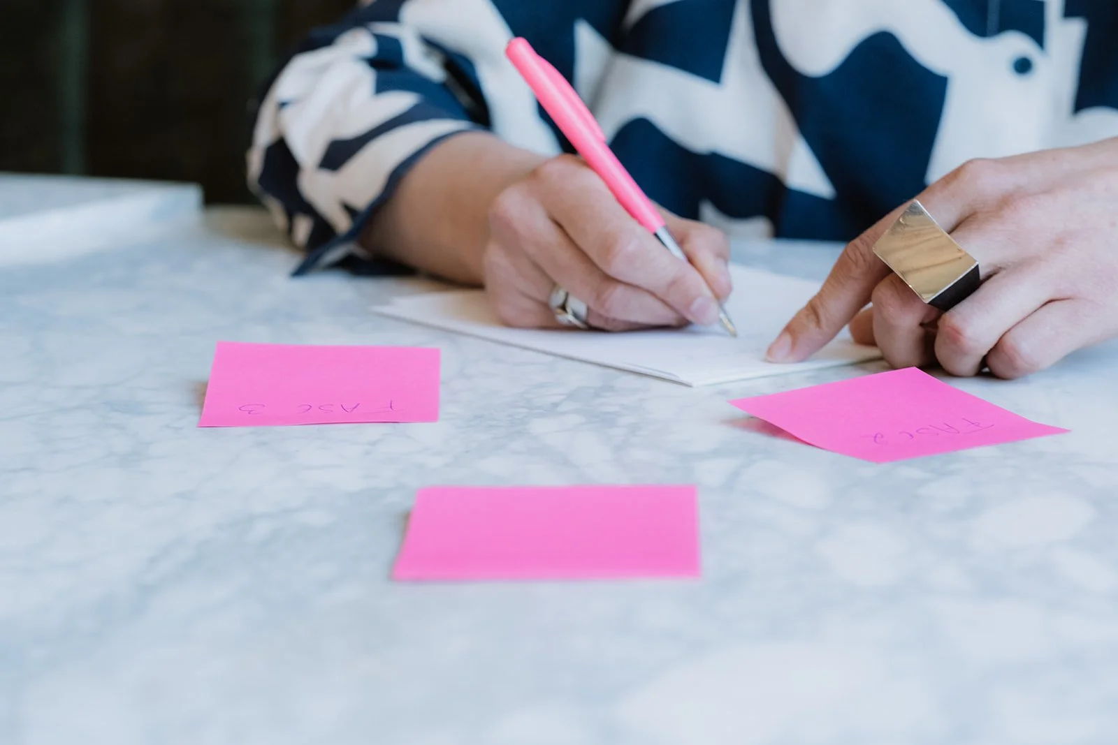 Persoon die aantekeningen maakt met een roze pen en post-its op een marmeren tafel.