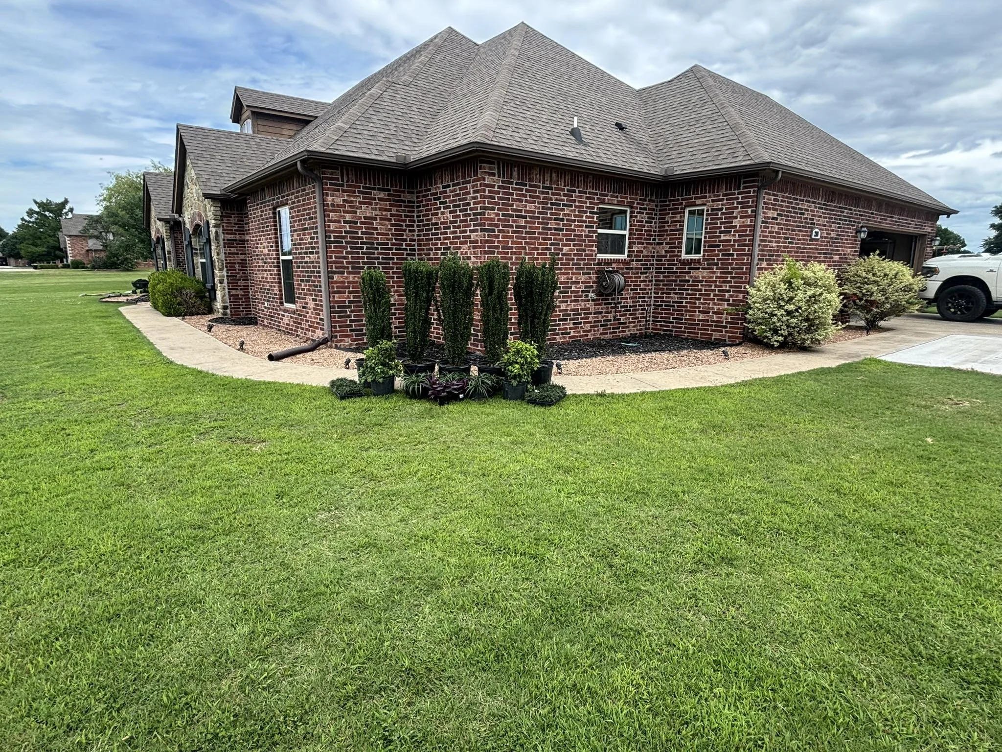 Landscape installation in Stroud, Oklahoma, featuring Sky Pencil Japanese Hollies, Purple Hearts, Dwarf Mondo Grass, and Nandina Firepower. Designed to add clean lines, year-round color, and low-maintenance curb appeal.