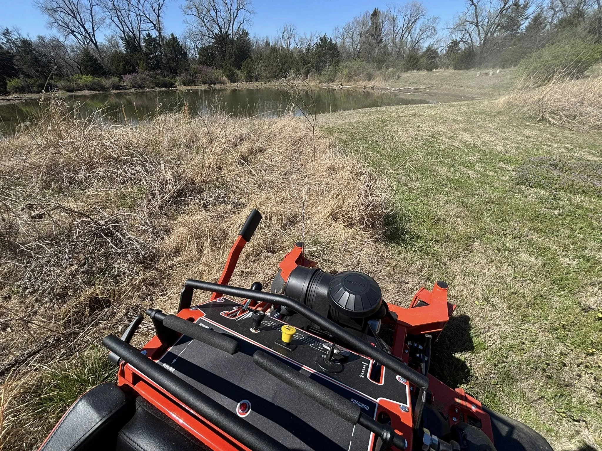 Professional bi-weekly lawn care service on a rural Cushing, OK property with pond, managing overgrowth and maintaining clean turf areas.