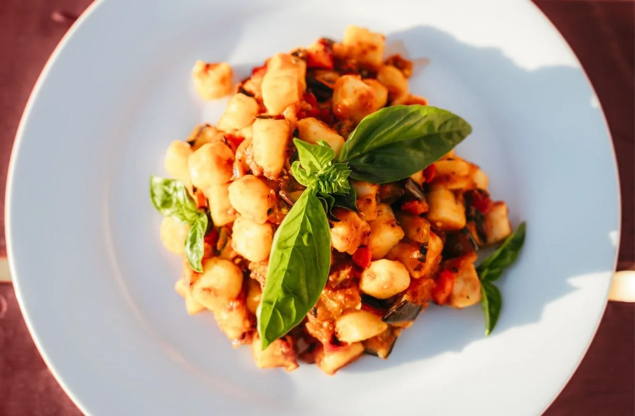 Plate of cooked gnocchi pasta with tomato sauce, garnished with fresh basil leaves.