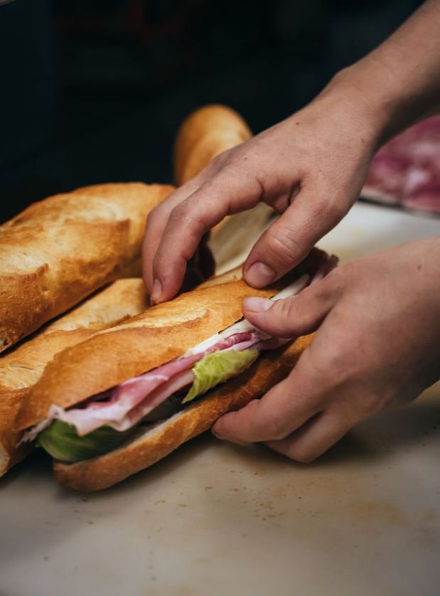 Person assembling a sandwich with ham, lettuce, and bread.
