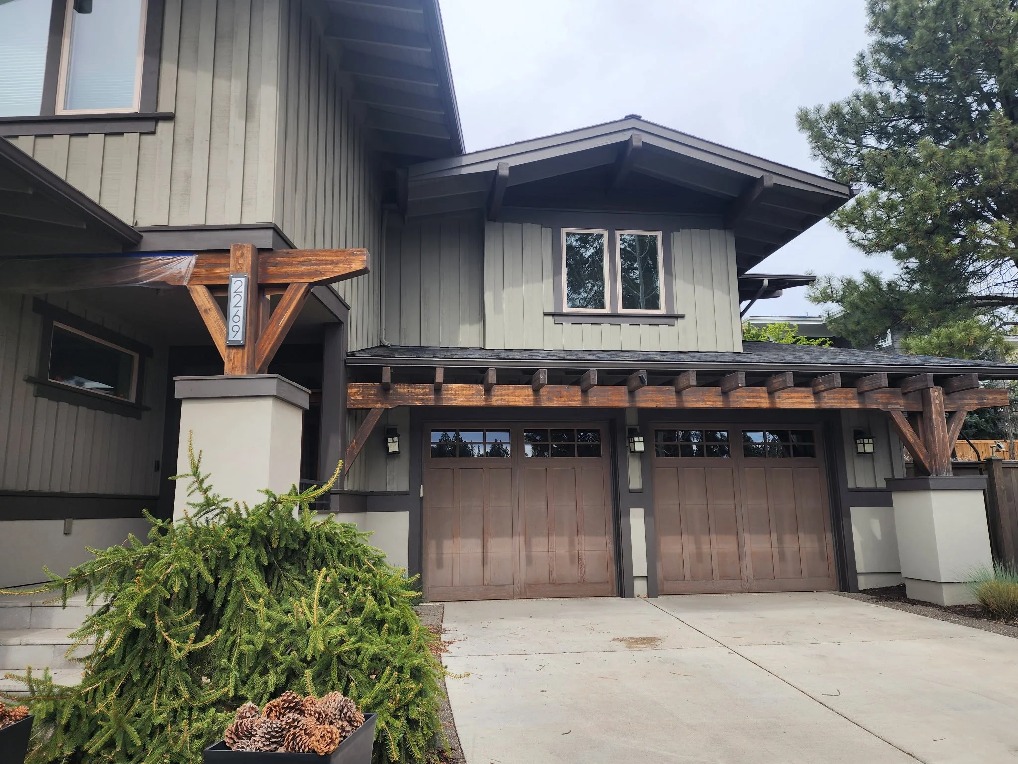 A modern house with a wooden overhang, gray siding, and large windows. There is a garage door below and a small evergreen bush in front. The house number 22609 is visible on a wooden beam.