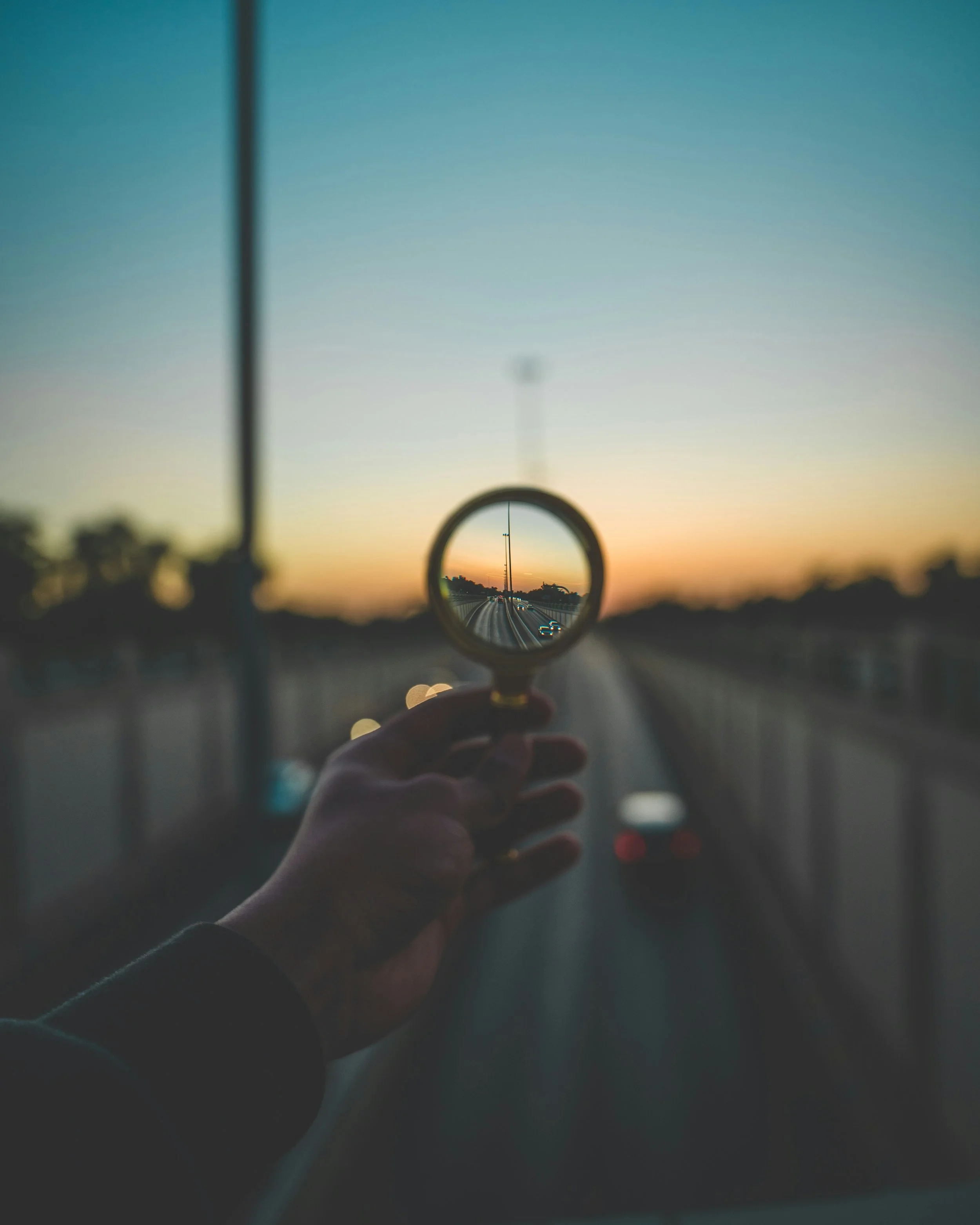 Person holding a mirror reflecting a road with cars at sunset