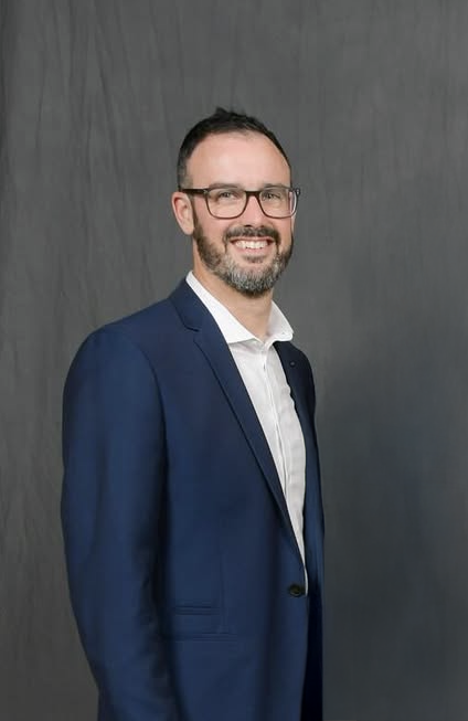 Image of Joel smiling at the camera in a blue suit