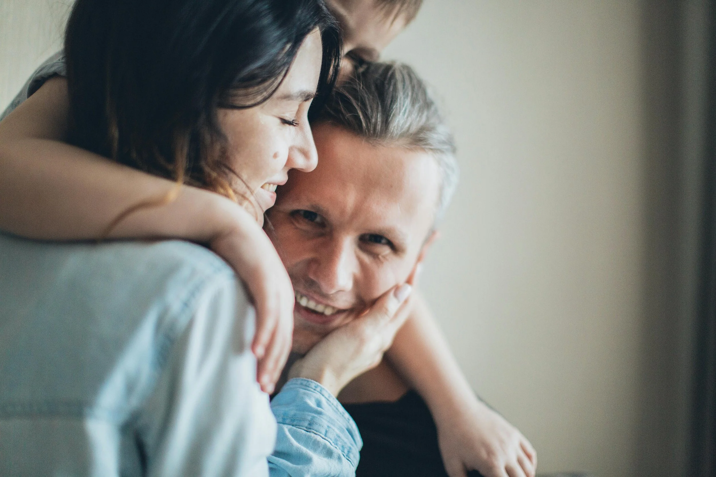 Three people are embracing each other and smiling happily indoors.