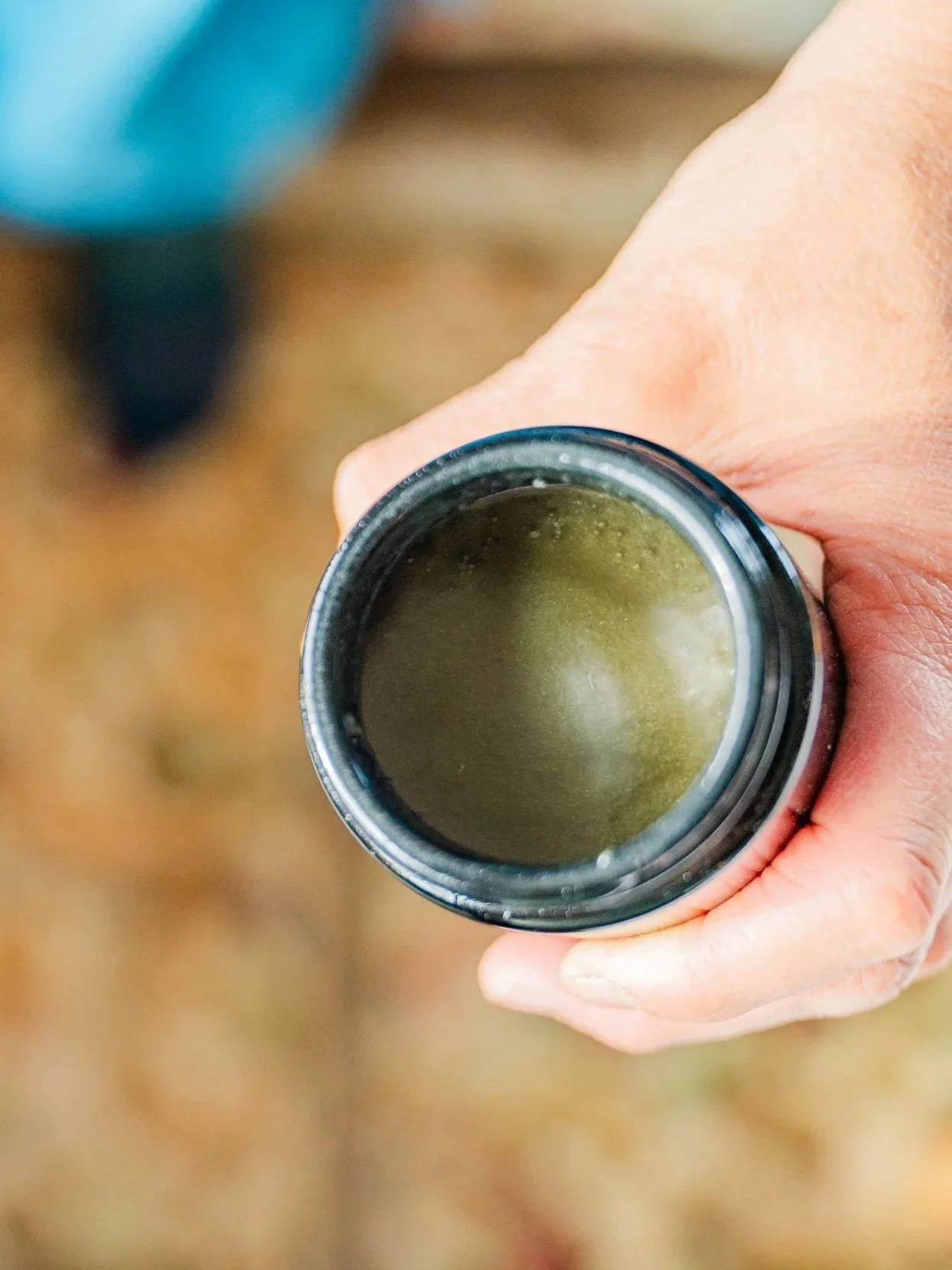 A hand holding an open container with a yellowish-green liquid inside