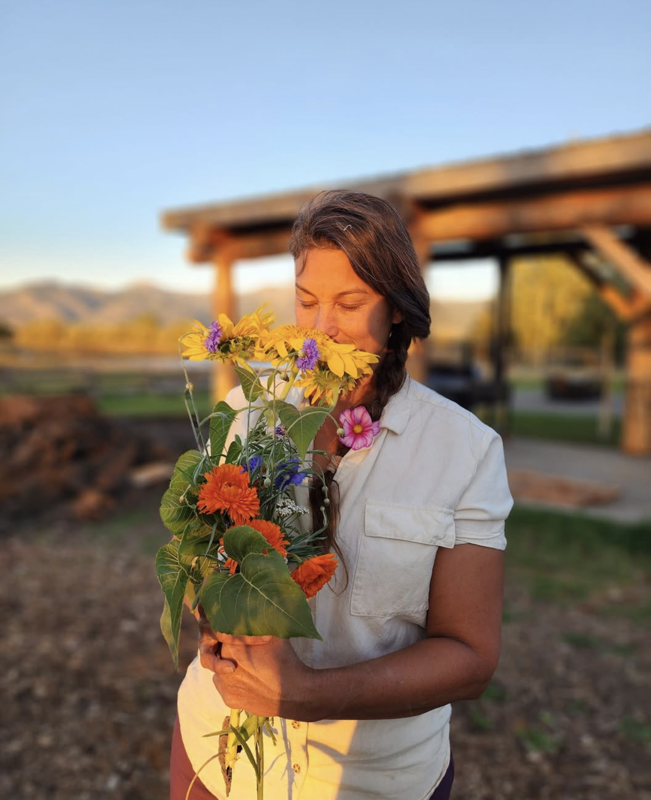 Woman holding a bouquet of colorful flowers outdoors during sunset.