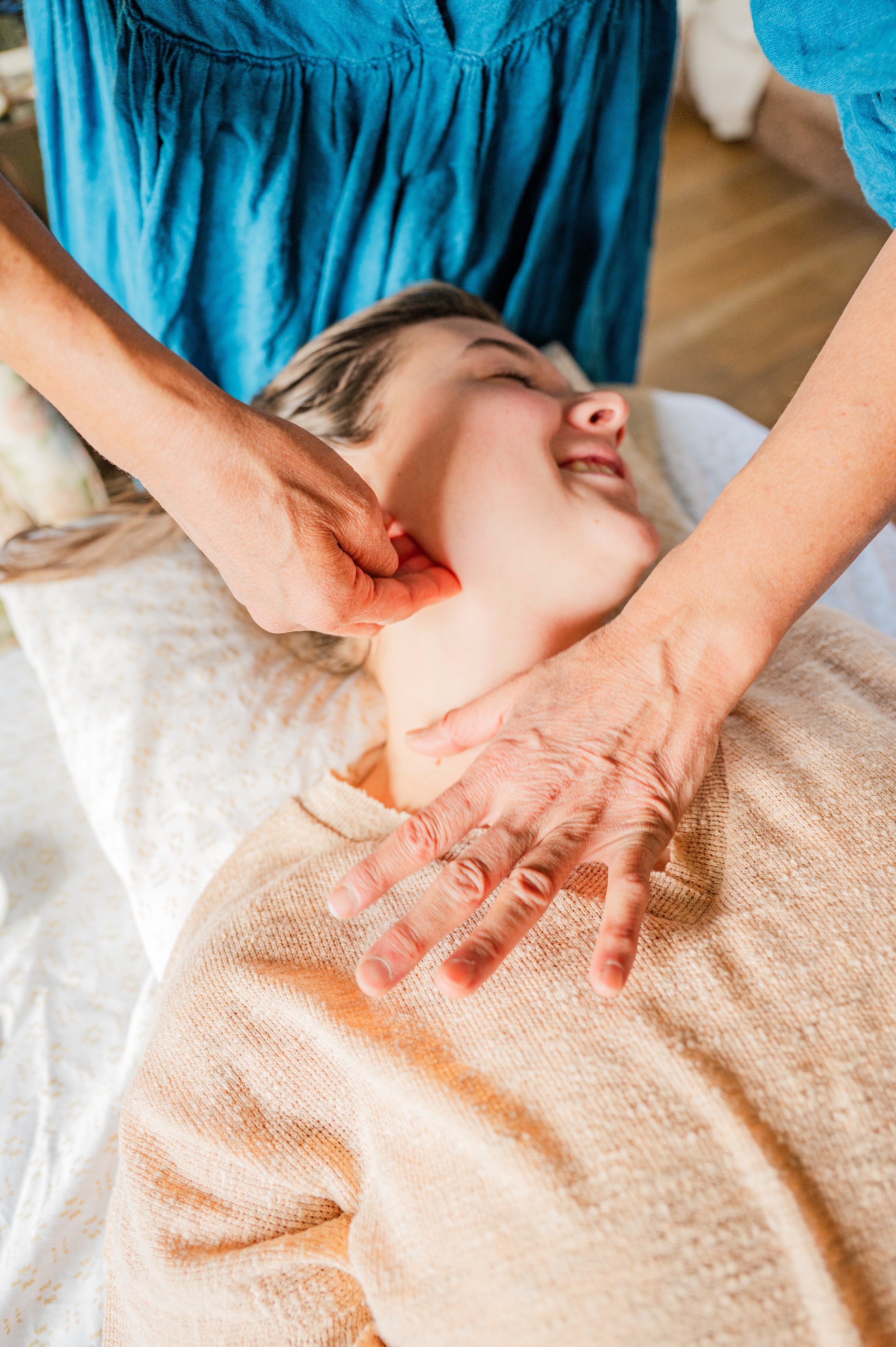 Person receiving a massage, lying on a bed with an older woman giving the massage.