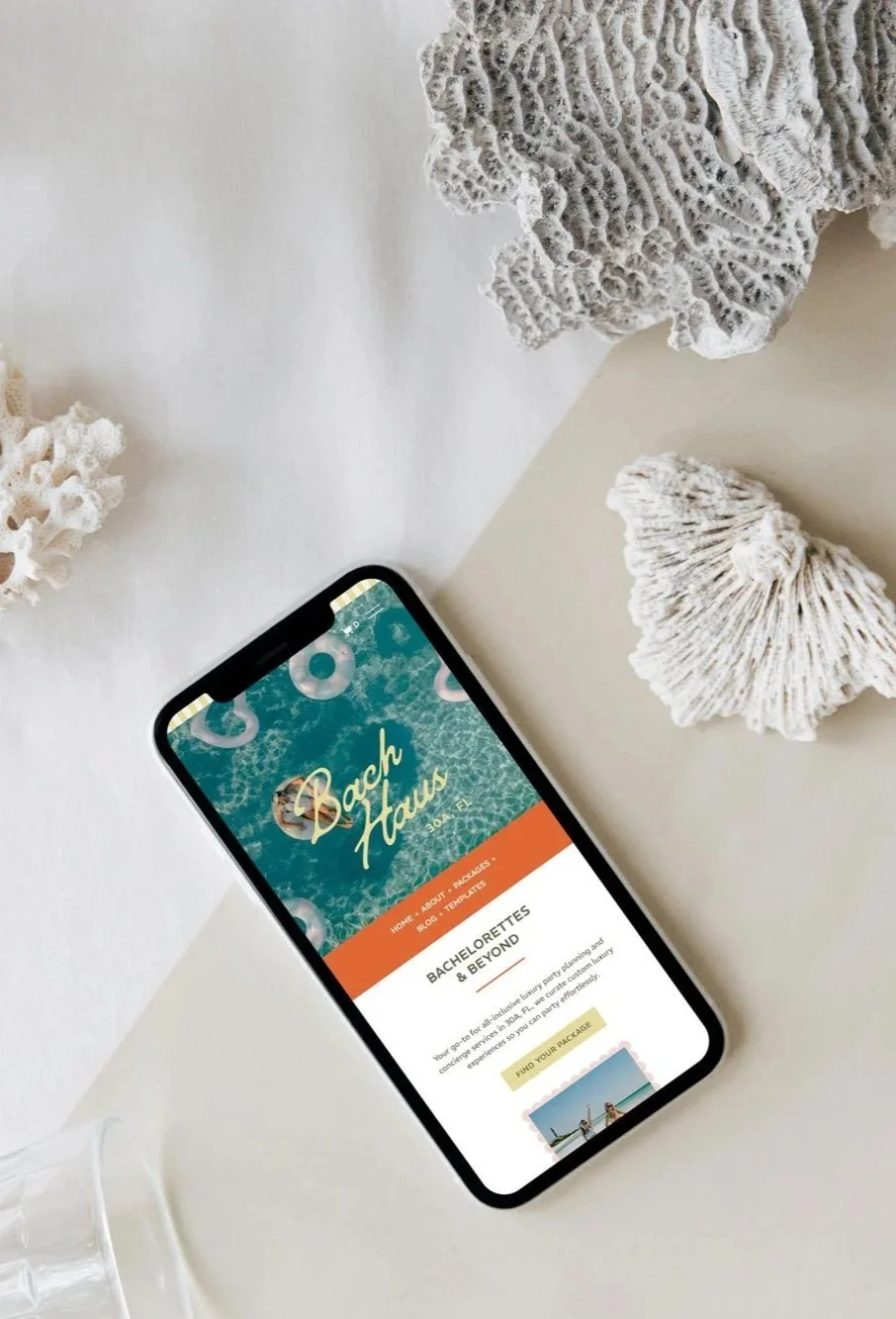 Smartphone displaying a travel website called 'Back HAU' on a white desk, surrounded by coral decorations.