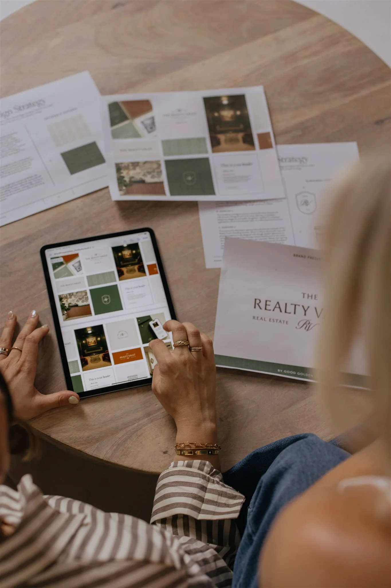 Person using tablet to browse real estate marketing materials on a wooden table.