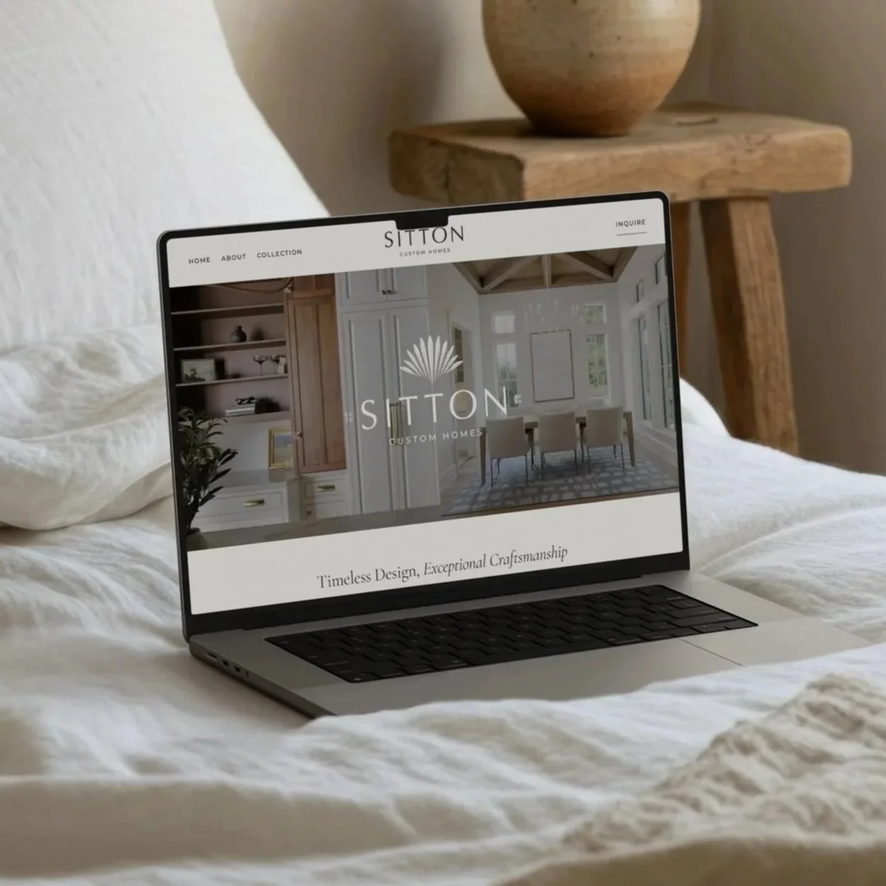 Open laptop on bed displaying a website for SITTON Custom Homes with an interior home image and tagline.