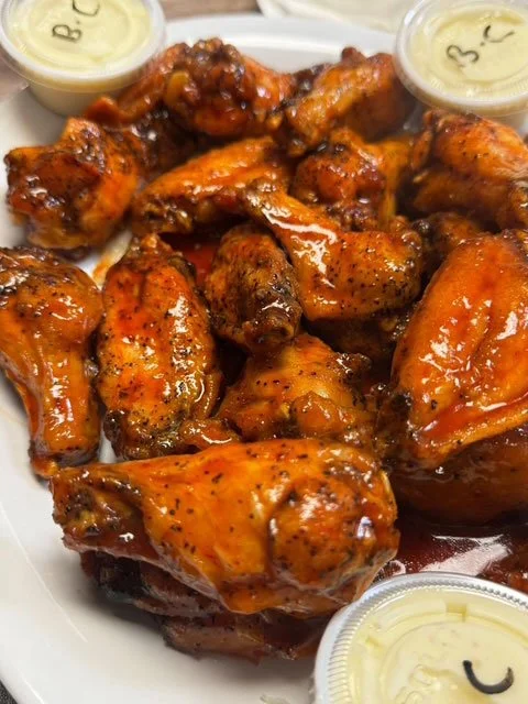 Plate of glazed buffalo chicken wings with three small containers of white dipping sauce.