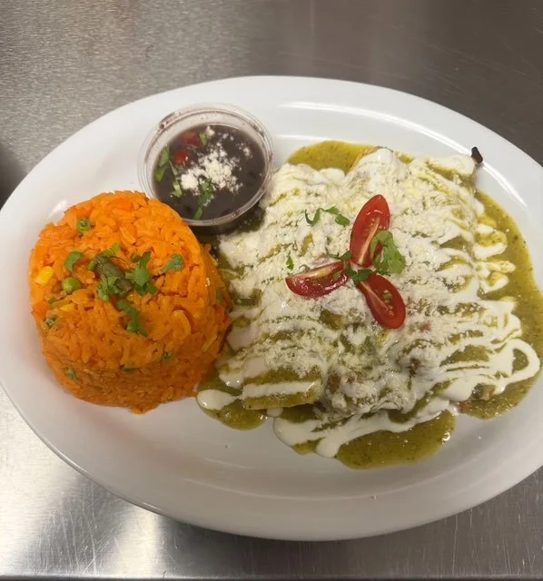Plate of Mexican dish with stuffed pepper covered in white sauce, a side of Mexican rice, and a small cup of dark sauce with chopped cilantro on a white oval plate.