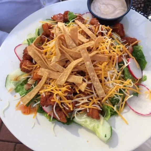 Crispy chicken taco salad topped with shredded cheddar and Monterey Jack cheese, fried strips, and served with a side of creamy dressing.